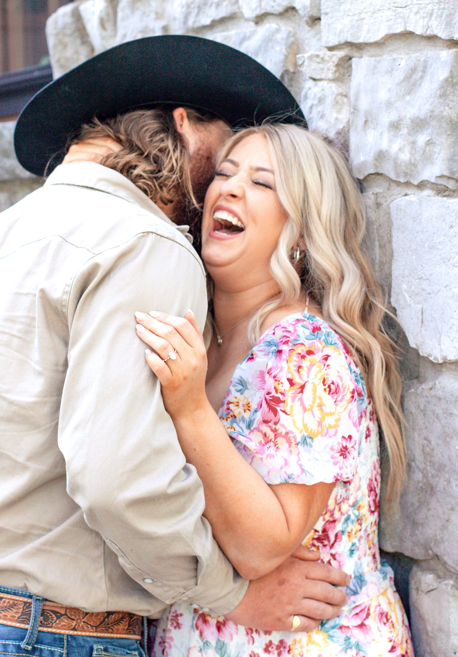 A romantic couple shares joyful laughter in a series of candid engagement photos against a stone wall.