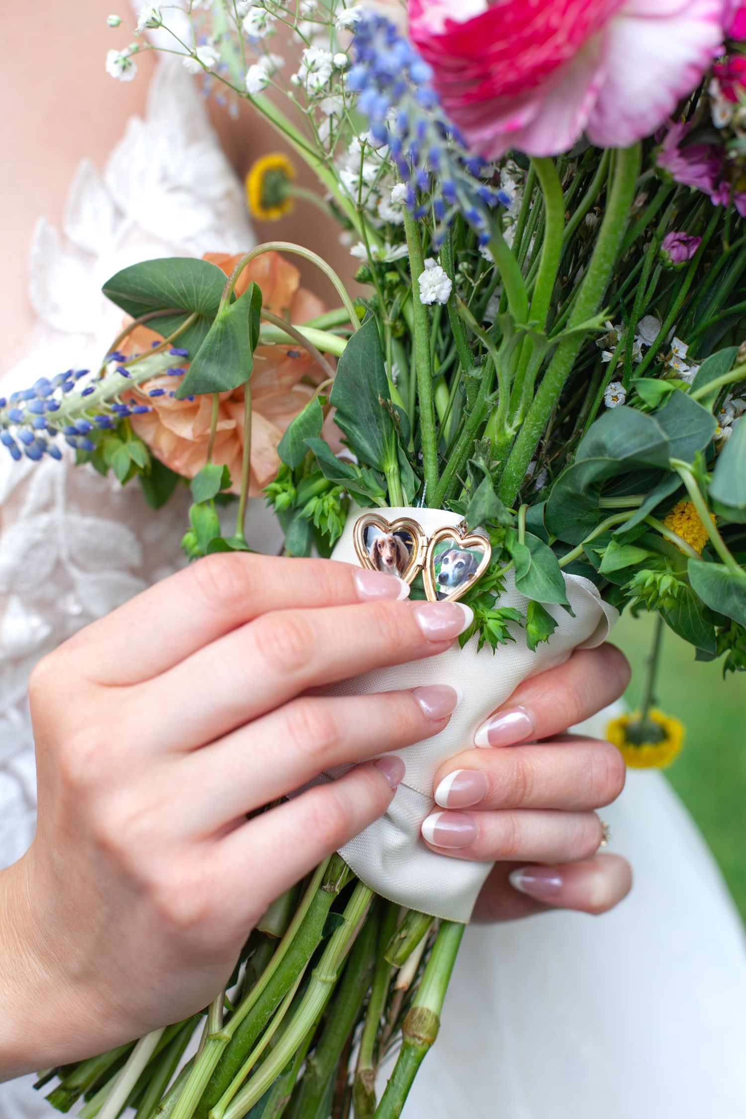 Close-up of a bride holding a colorful wildflower bouquet adorned with a gold heart-shaped locket charm.