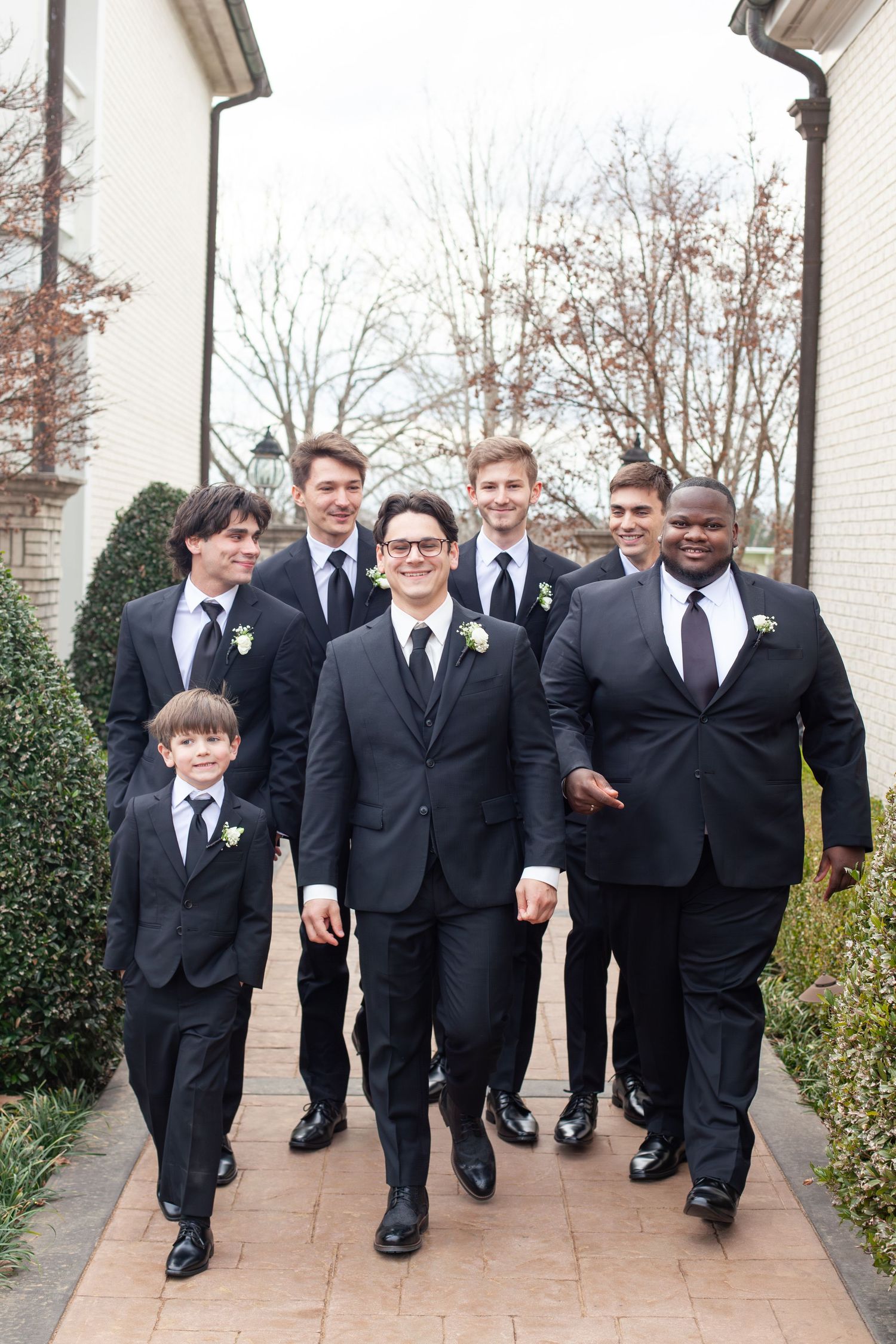 Groom and groomsmen in black suits with boutonnieres walking together outdoors at a wedding ceremony.
