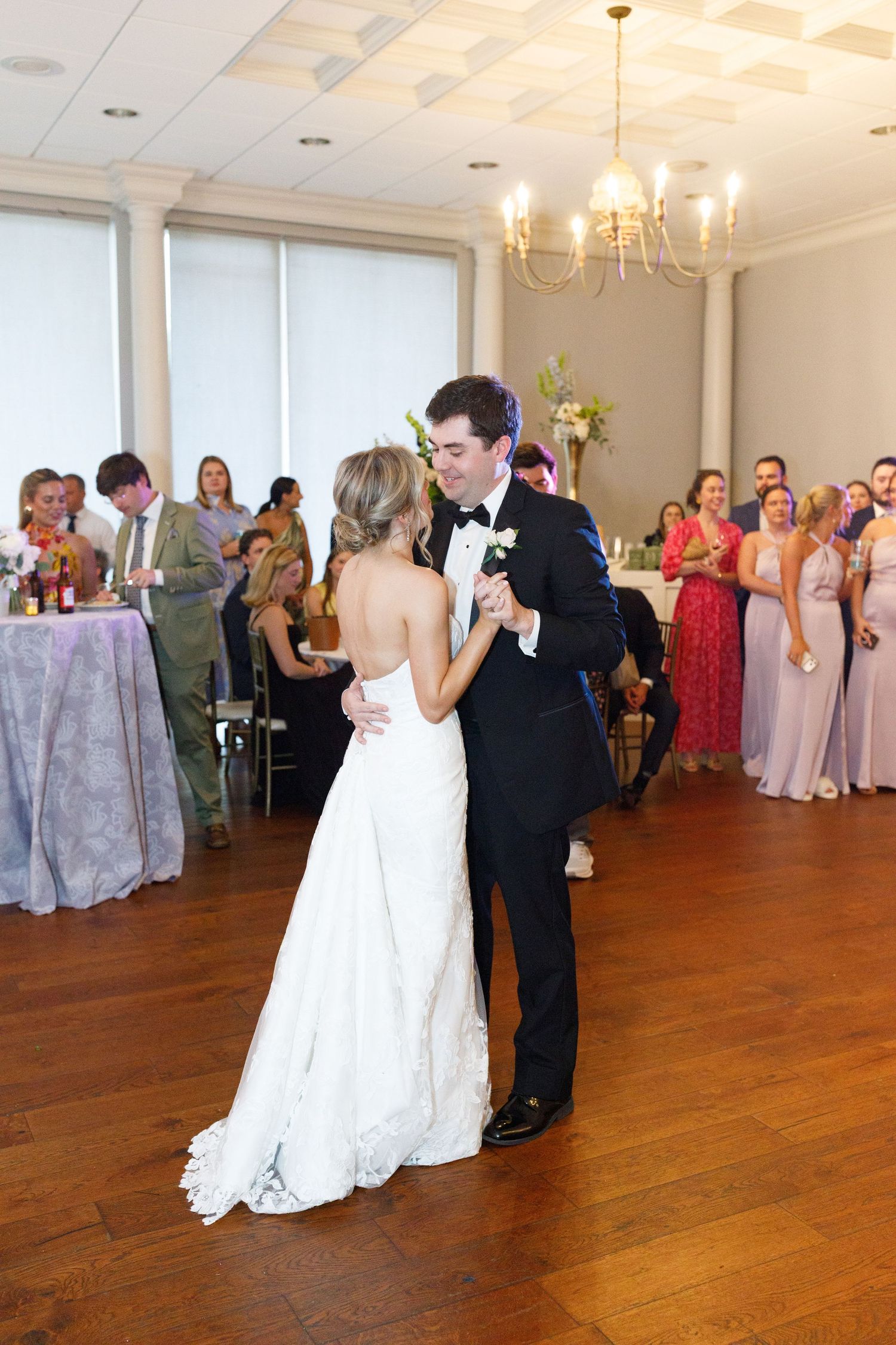 Bride and groom share their first dance in an elegant ballroom surrounded by wedding guests.
