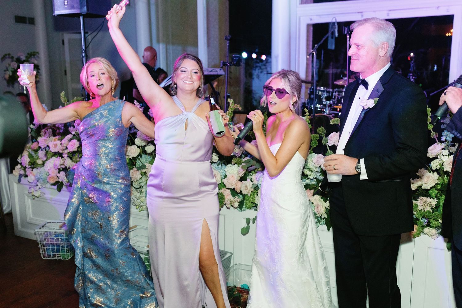 Joyful wedding reception with bride and guests dancing and celebrating in elegant floral venue.