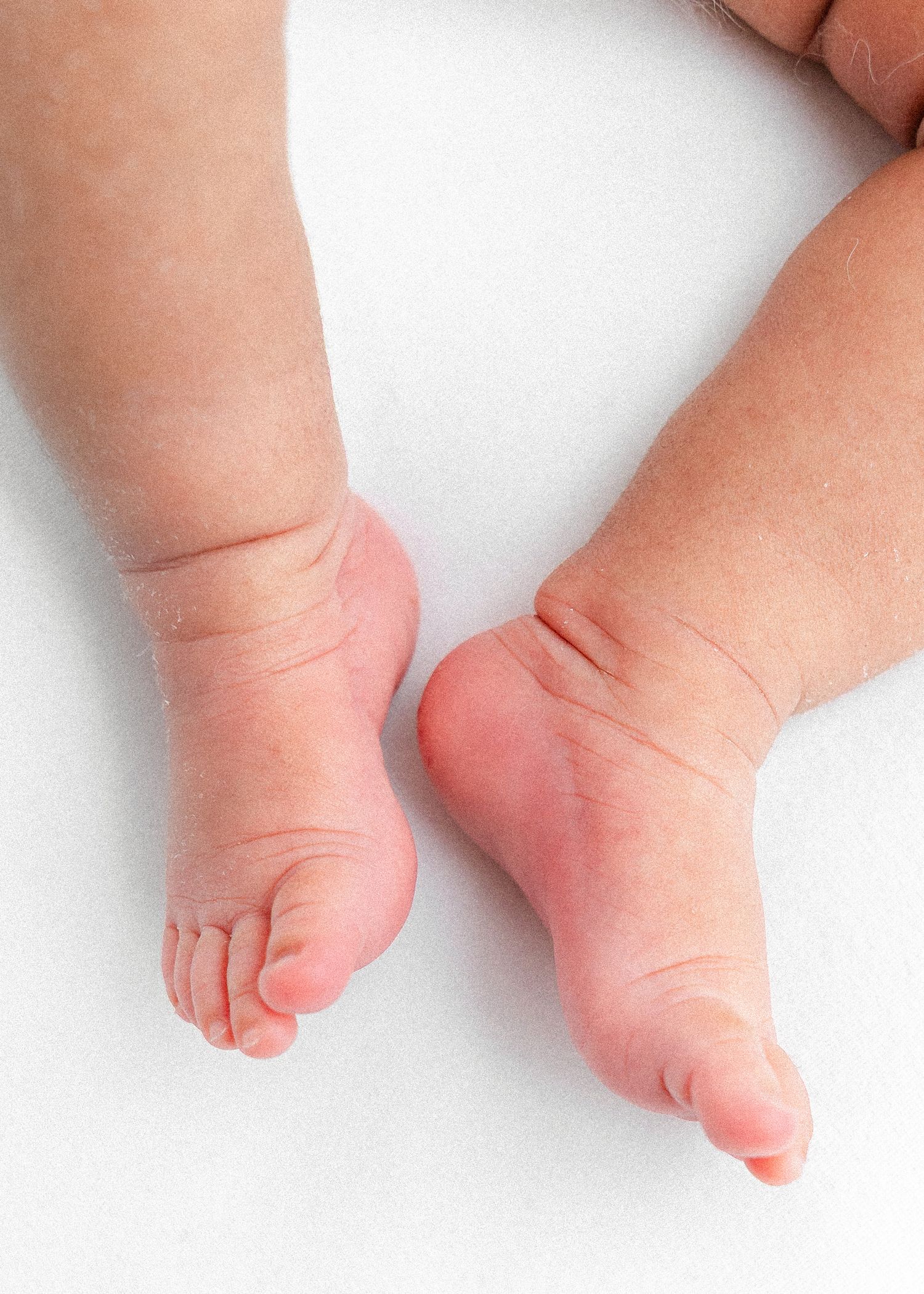 Close up of chubby baby feet with rosy pink soles on white surface.