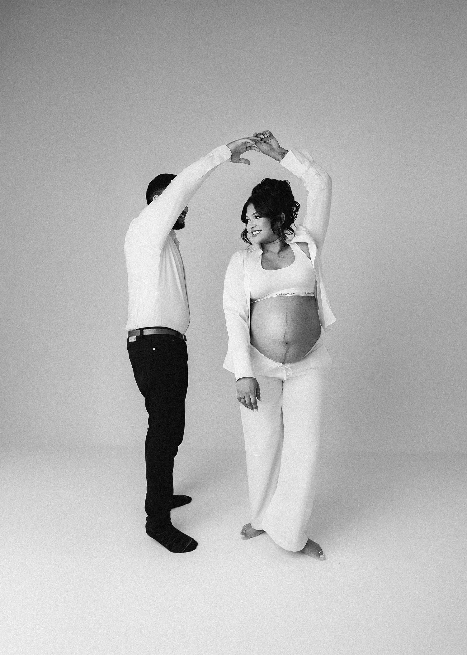 Black and white artistic maternity poses showing couple in minimalist studio setting.