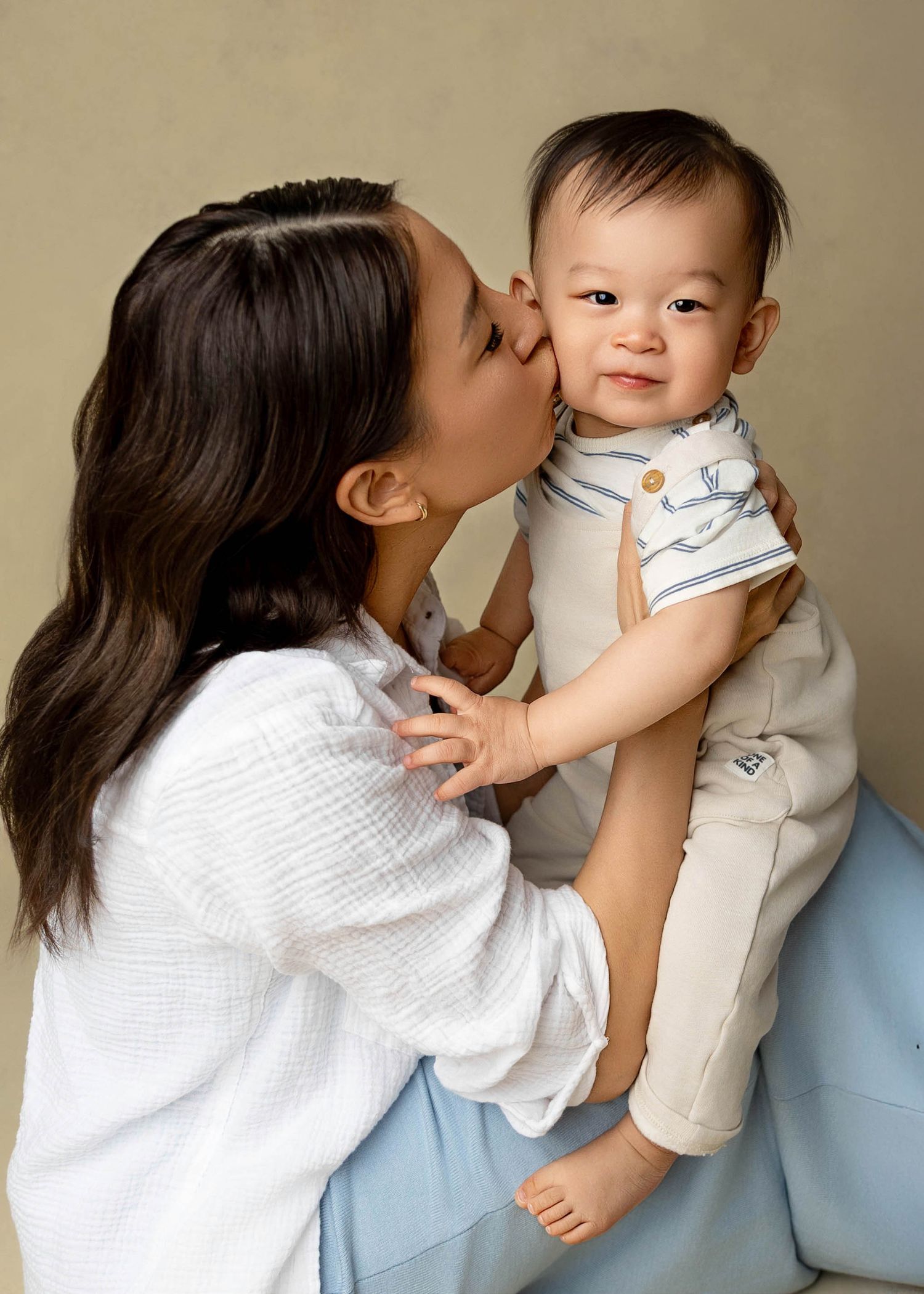 Sweet candid moments captured between a child and parent in white clothing against a neutral backdrop.
