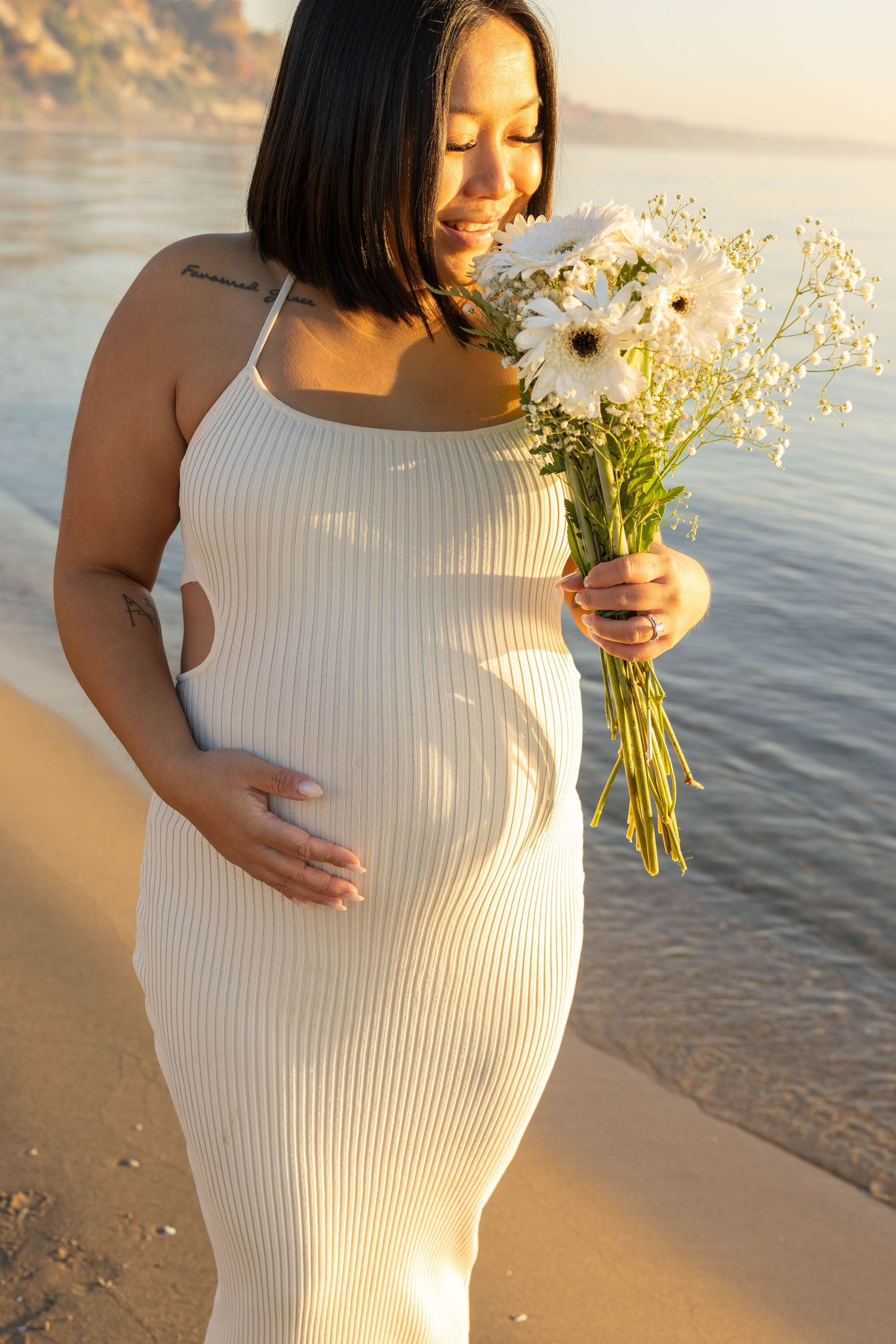 Sunset beach maternity photos with white ribbed dress and wildflower bouquet.
