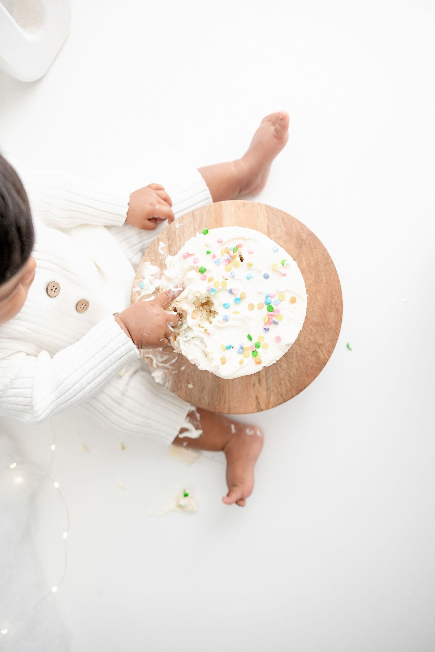Overhead view of baby enjoying cake during a white-themed smash cake session.