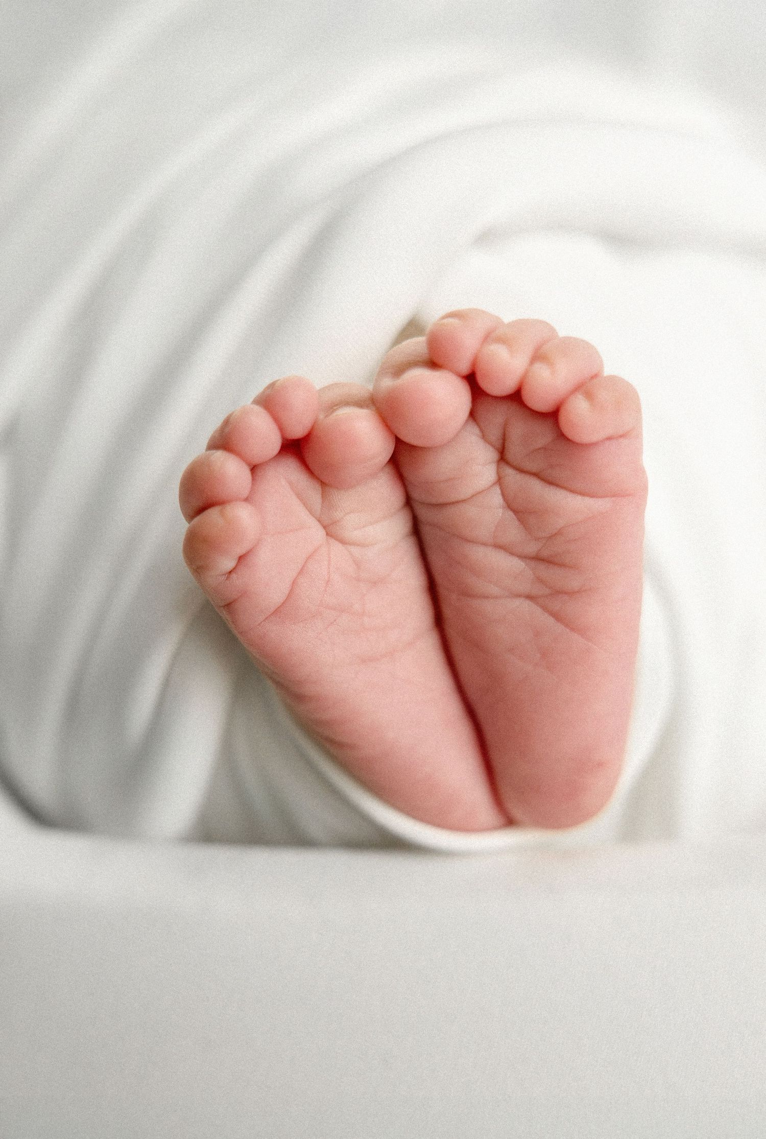 Delicate newborn baby feet and toes against white bedding.