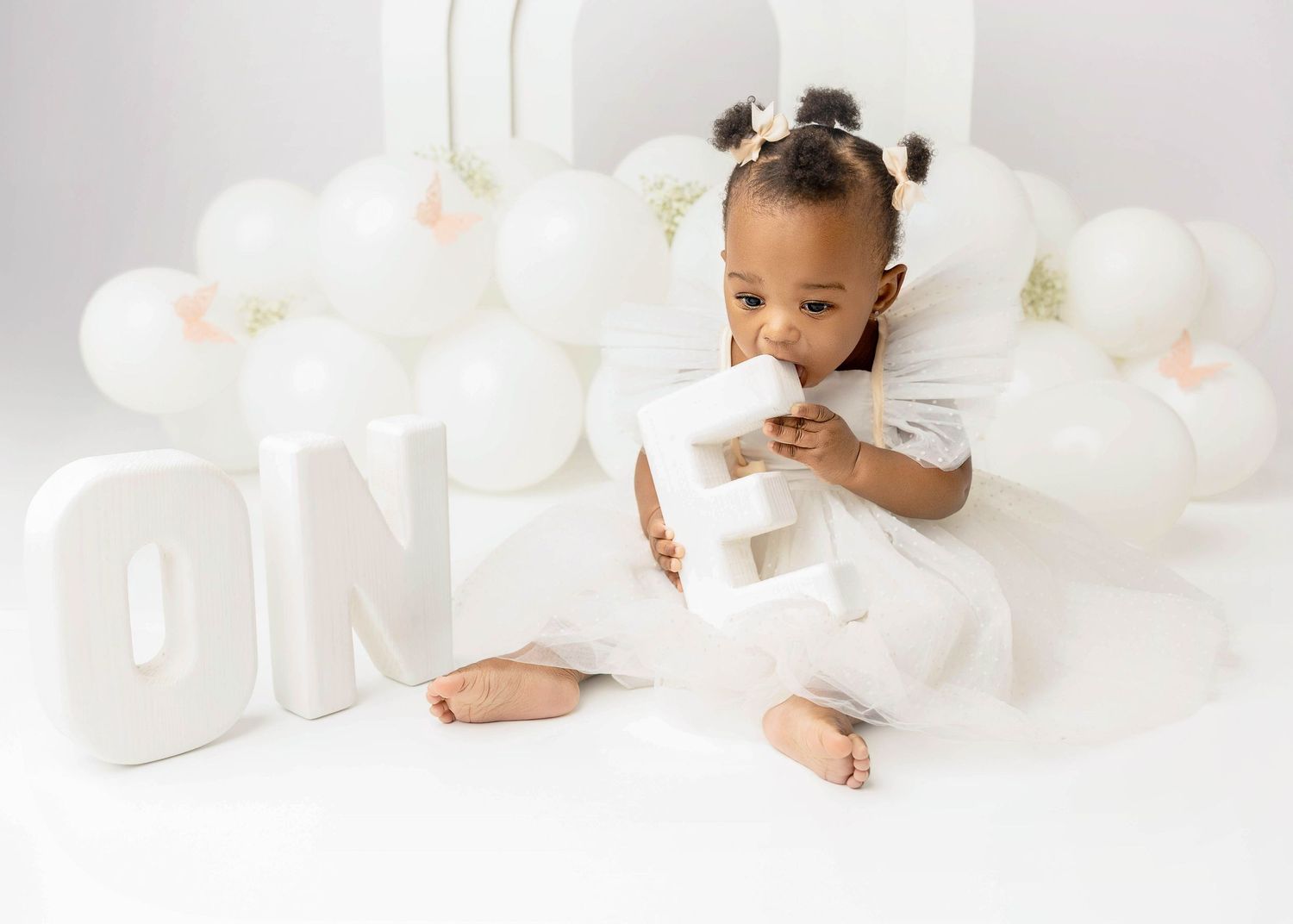 White minimalist baby photoshoot with soft cloud-like decorations and white balloons.