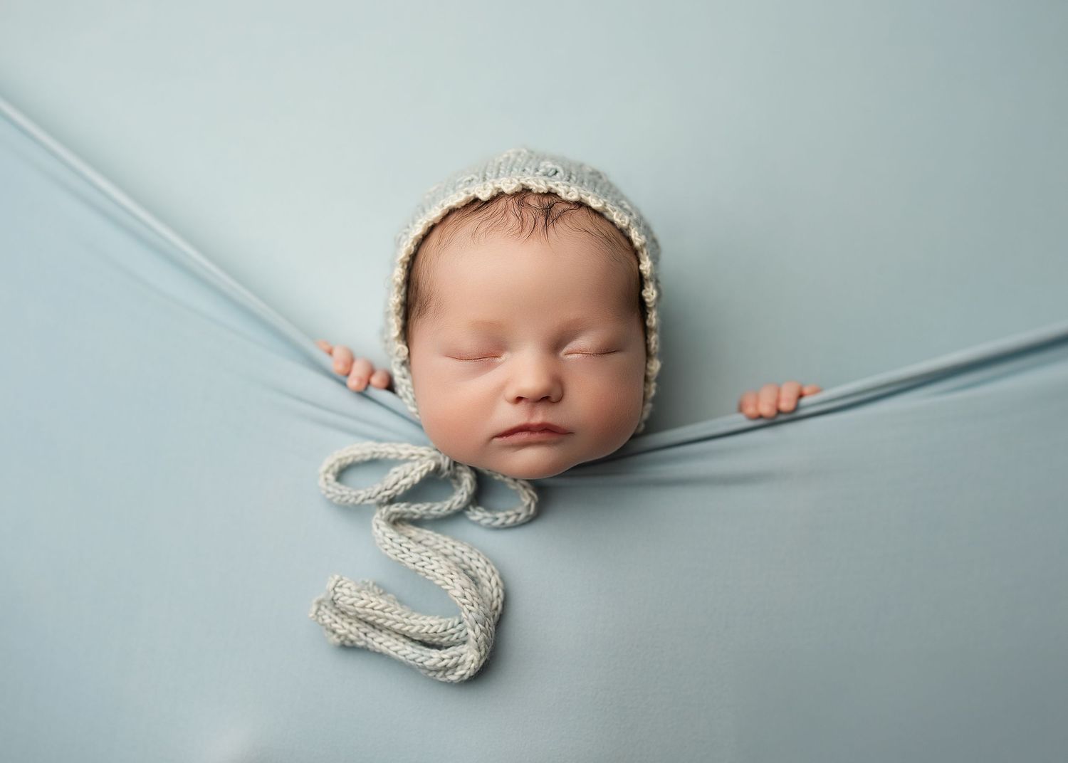 Sleeping newborn wrapped in gray fabric on light blue background in minimalist portrait style.