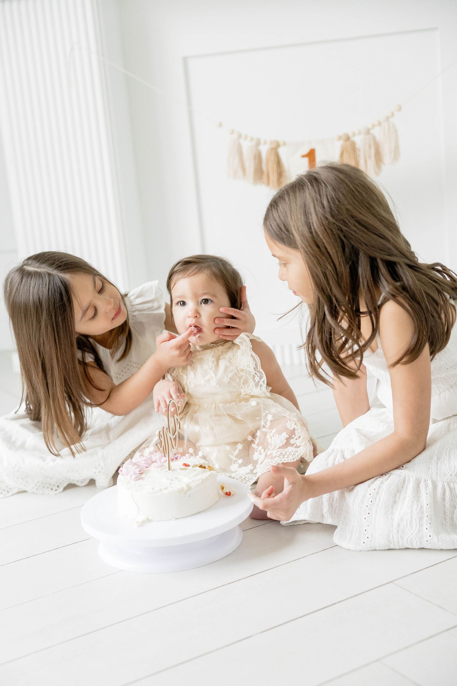 Series of photos showing baby in white dress playing with cake on white floor.