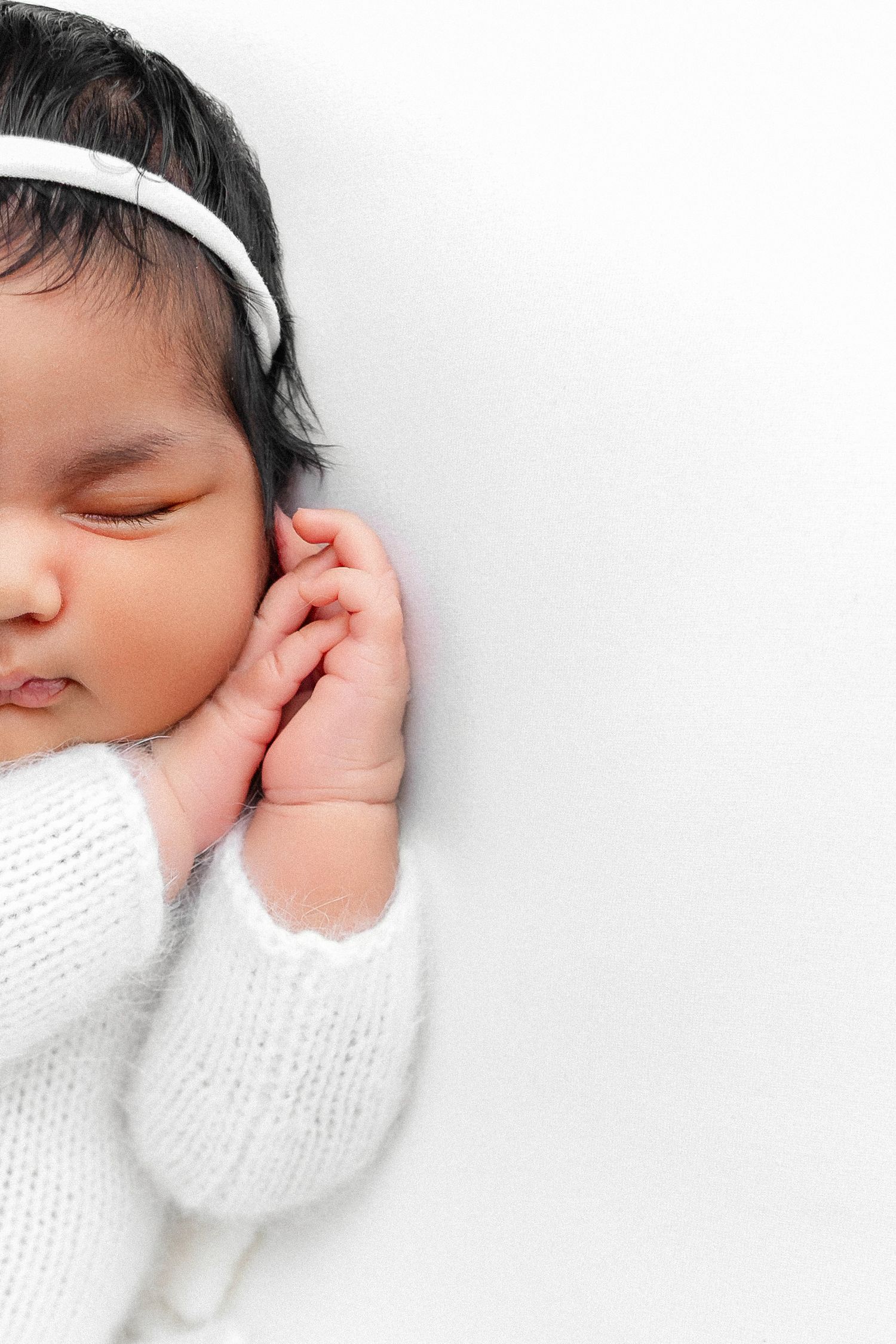 Peaceful sleeping infant in white knit sweater with hand near face.