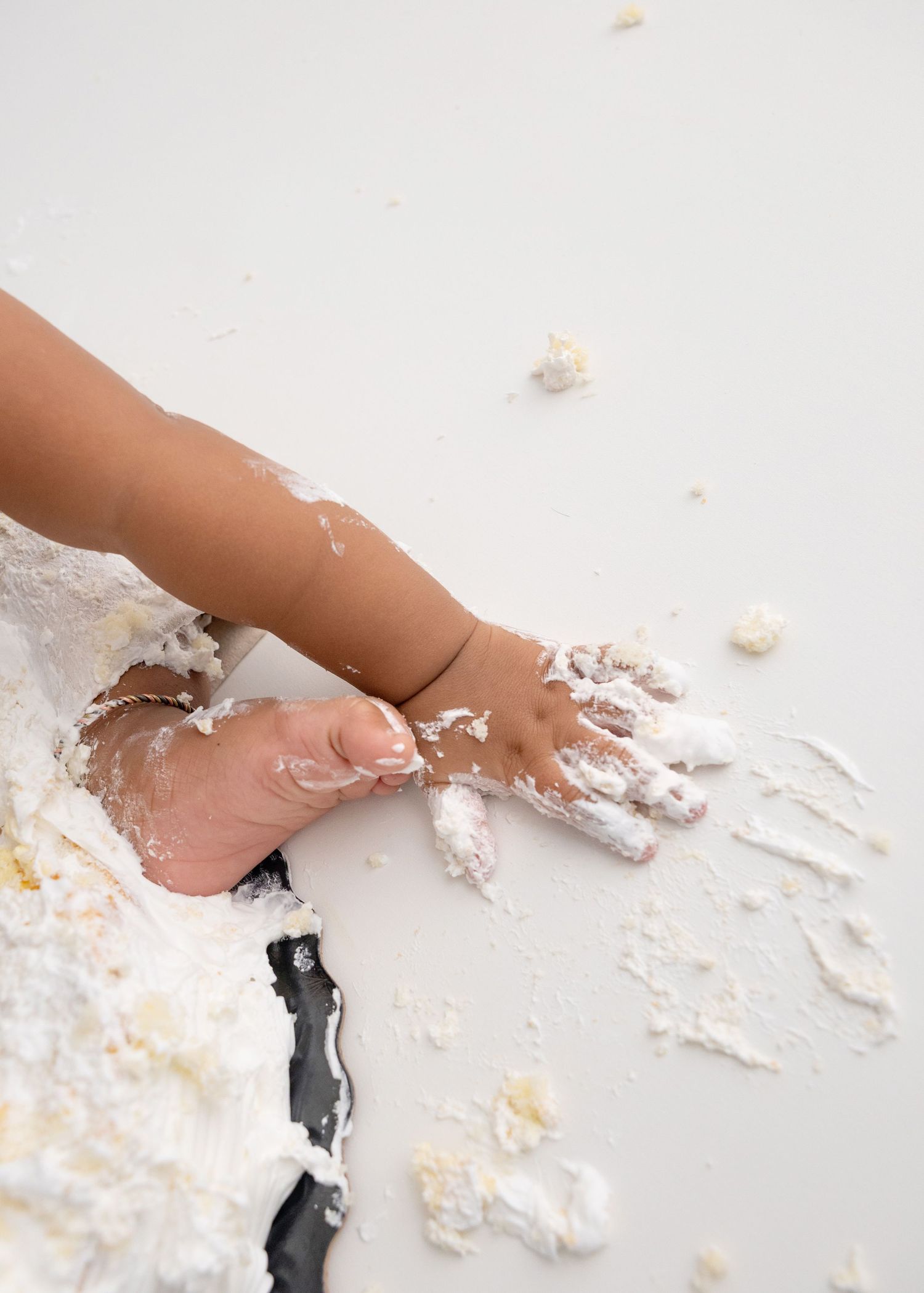 Close-up of small hands playing with cake smash mess on white surface.