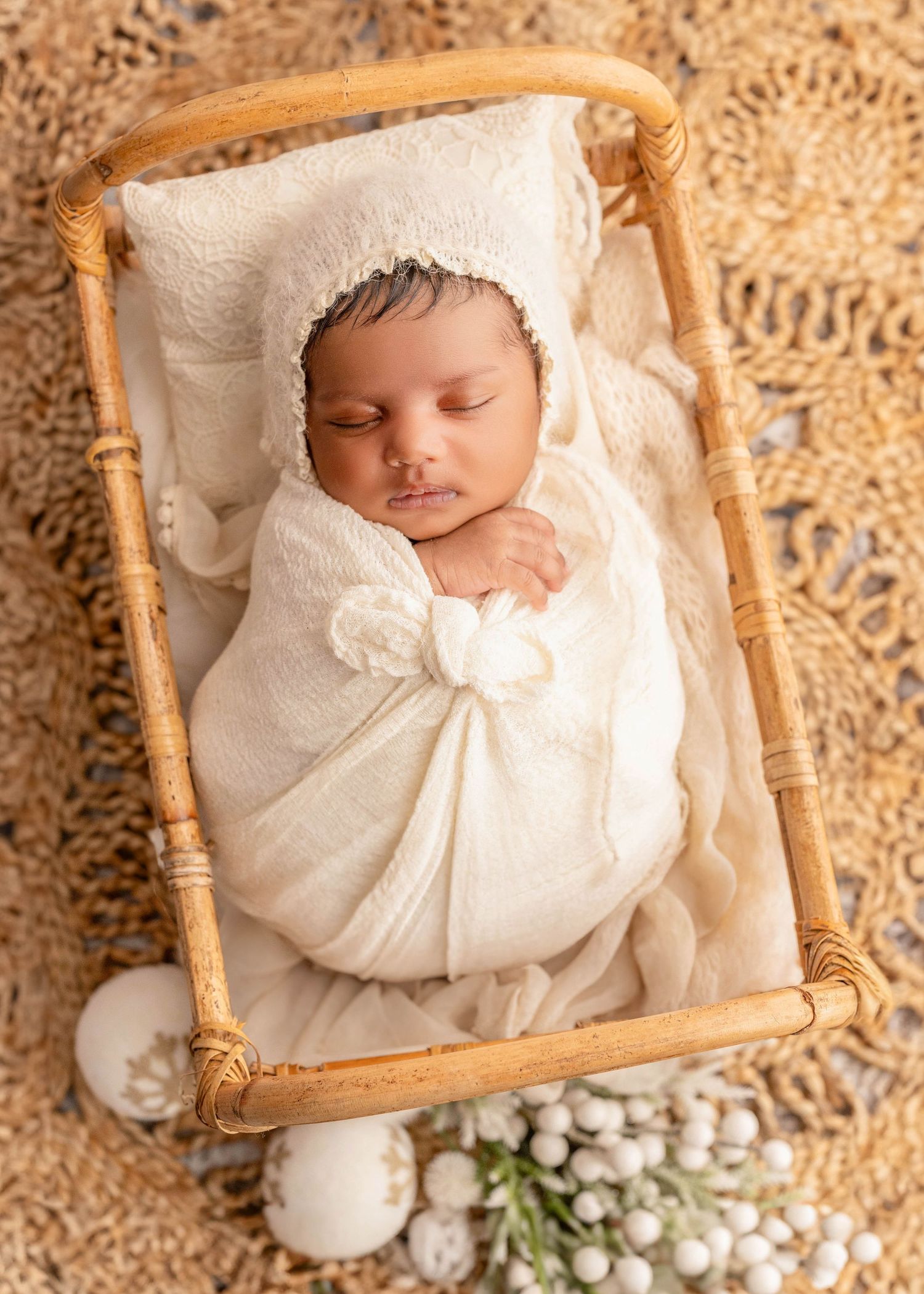 Sleeping newborn wrapped in white blanket resting in wooden basket with delicate floral accents.