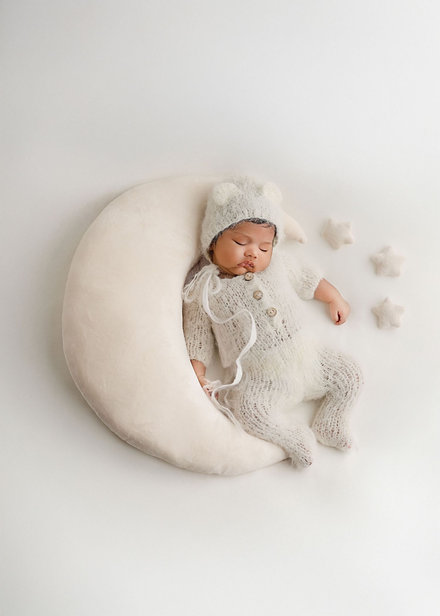 Newborn sleeping peacefully on curved white pillow wearing knit bonnet.