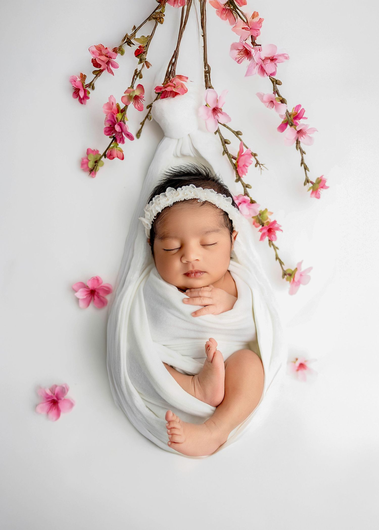 Newborn photography with cherry blossom branches and white fabric styling.