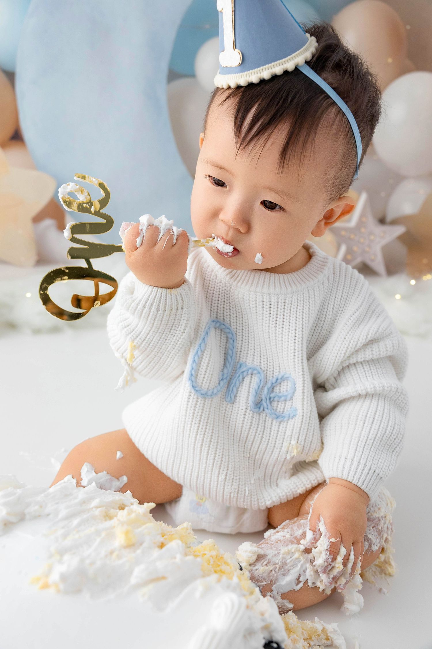 Baby in white sweater playing with cake and decorations during a celebration.