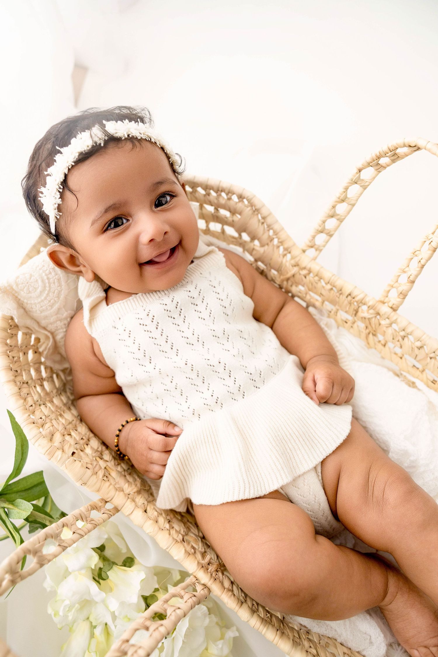 Baby in white dress lying in woven basket with floral decorations.