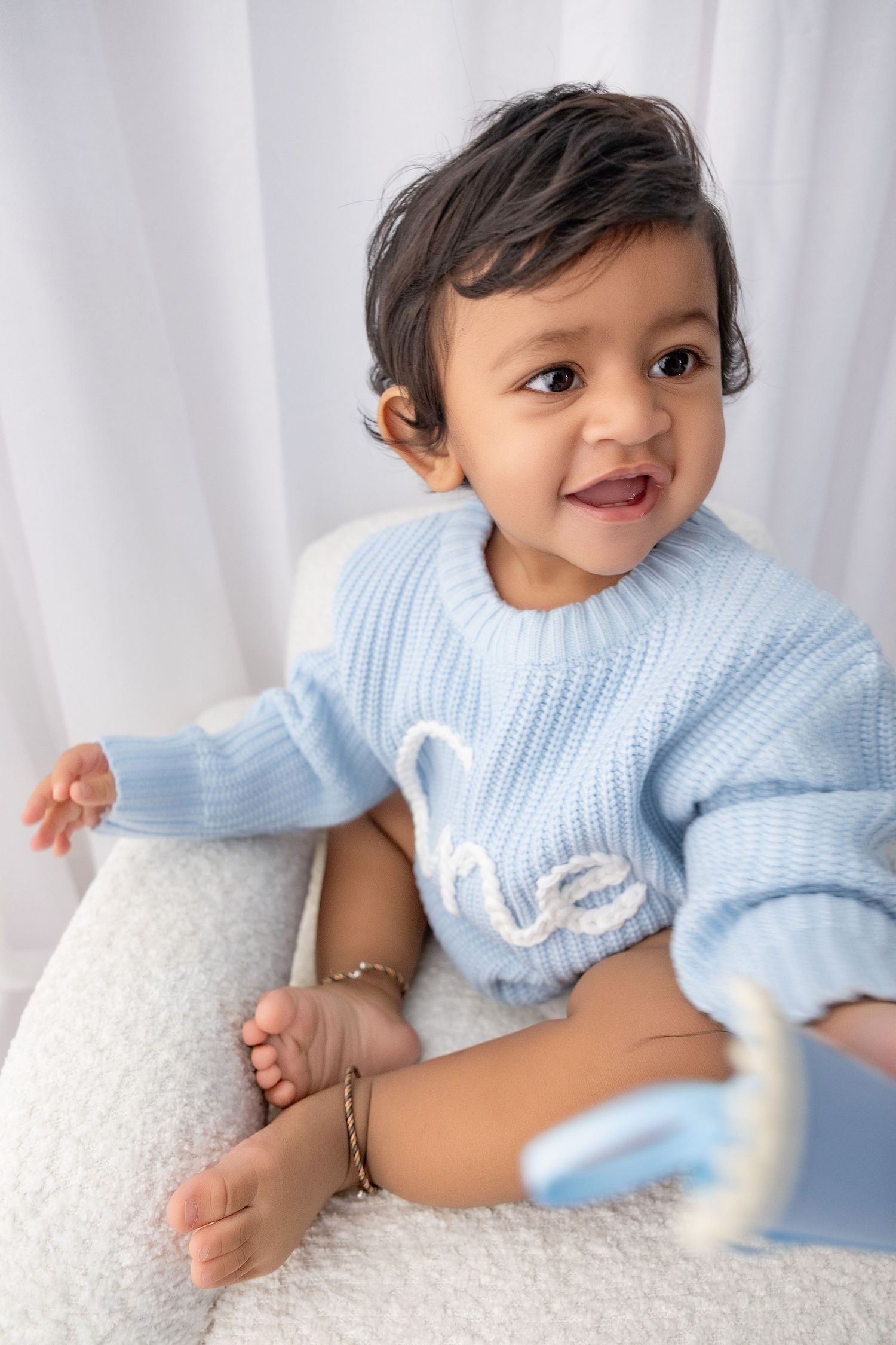 Baby in light blue sweater posing against white backdrop during photoshoot.
