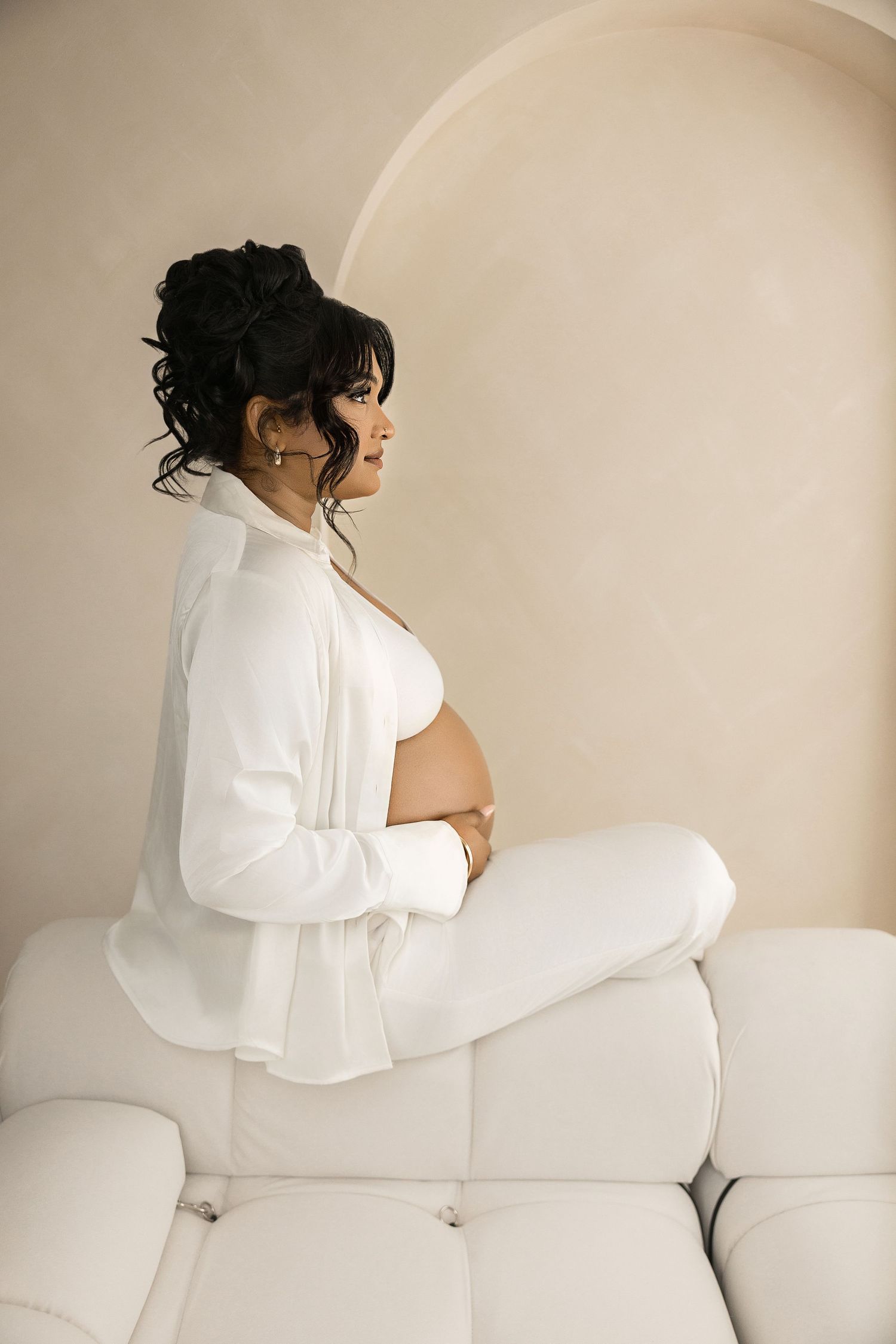 Modern maternity portraits on white couch showing pregnancy silhouette in casual attire.
