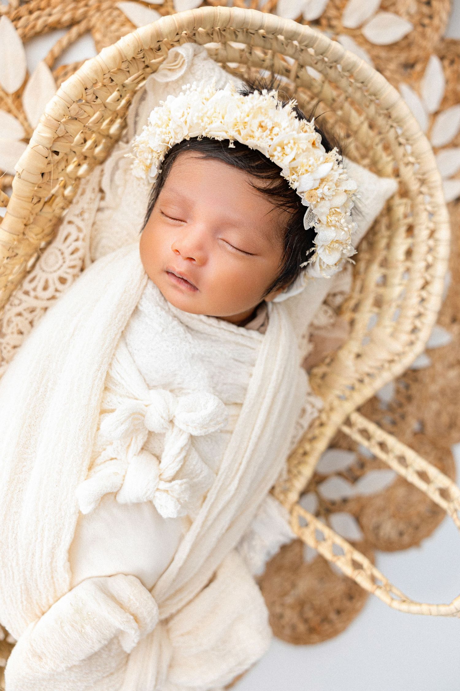 Sleeping newborn in white outfit and bonnet lying in woven basket.
