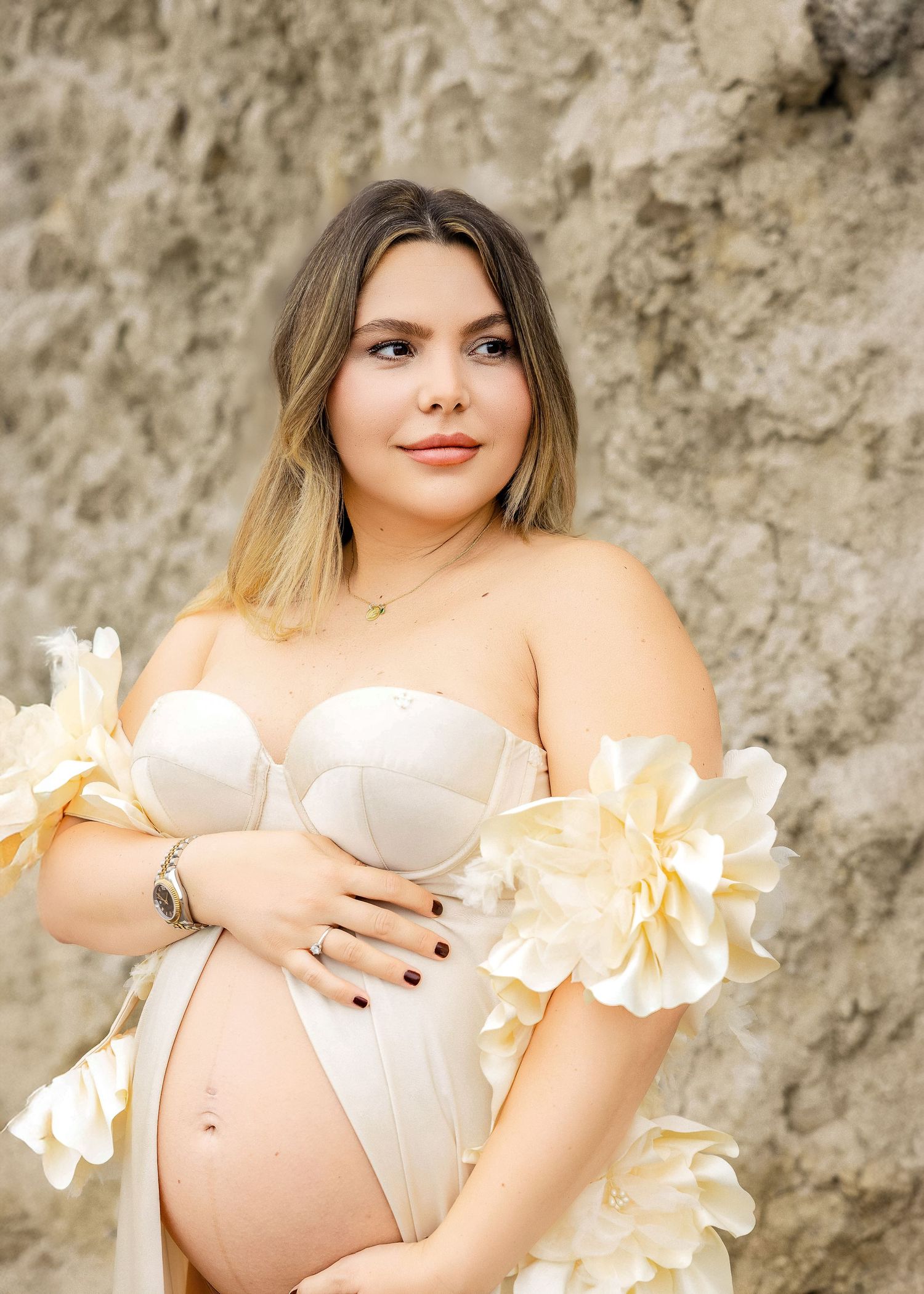 Maternity photo shoot featuring delicate white flowers against a textured stone background.