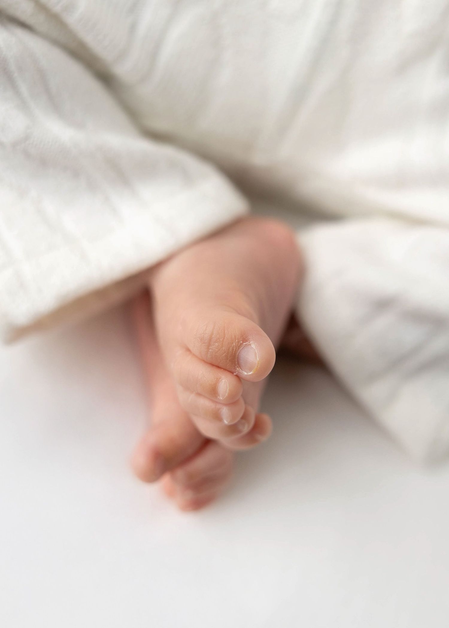 Series of delicate baby toes peeking out from white blanket.