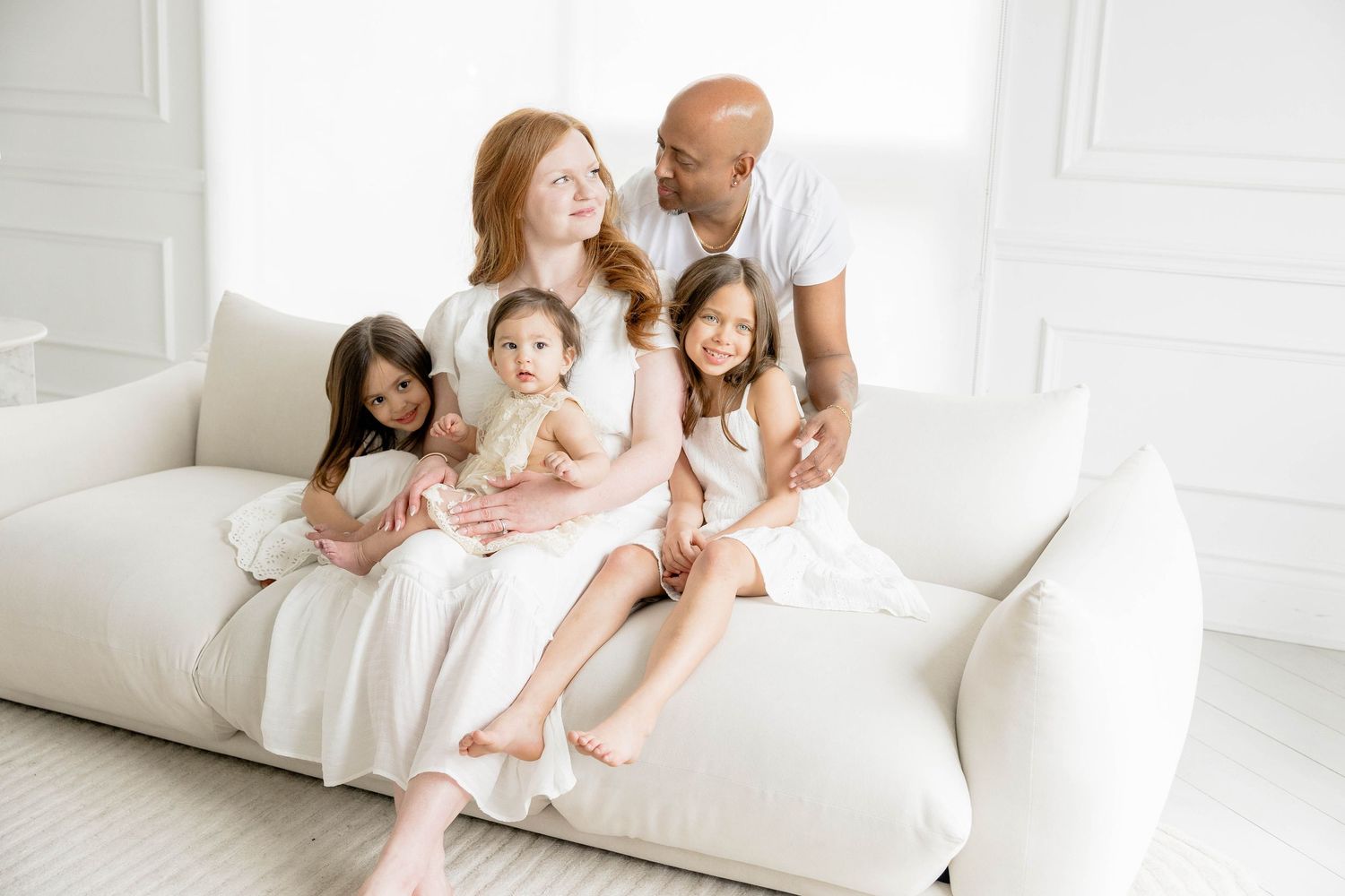 Bright family lifestyle photos captured on a white couch in a minimalist setting.