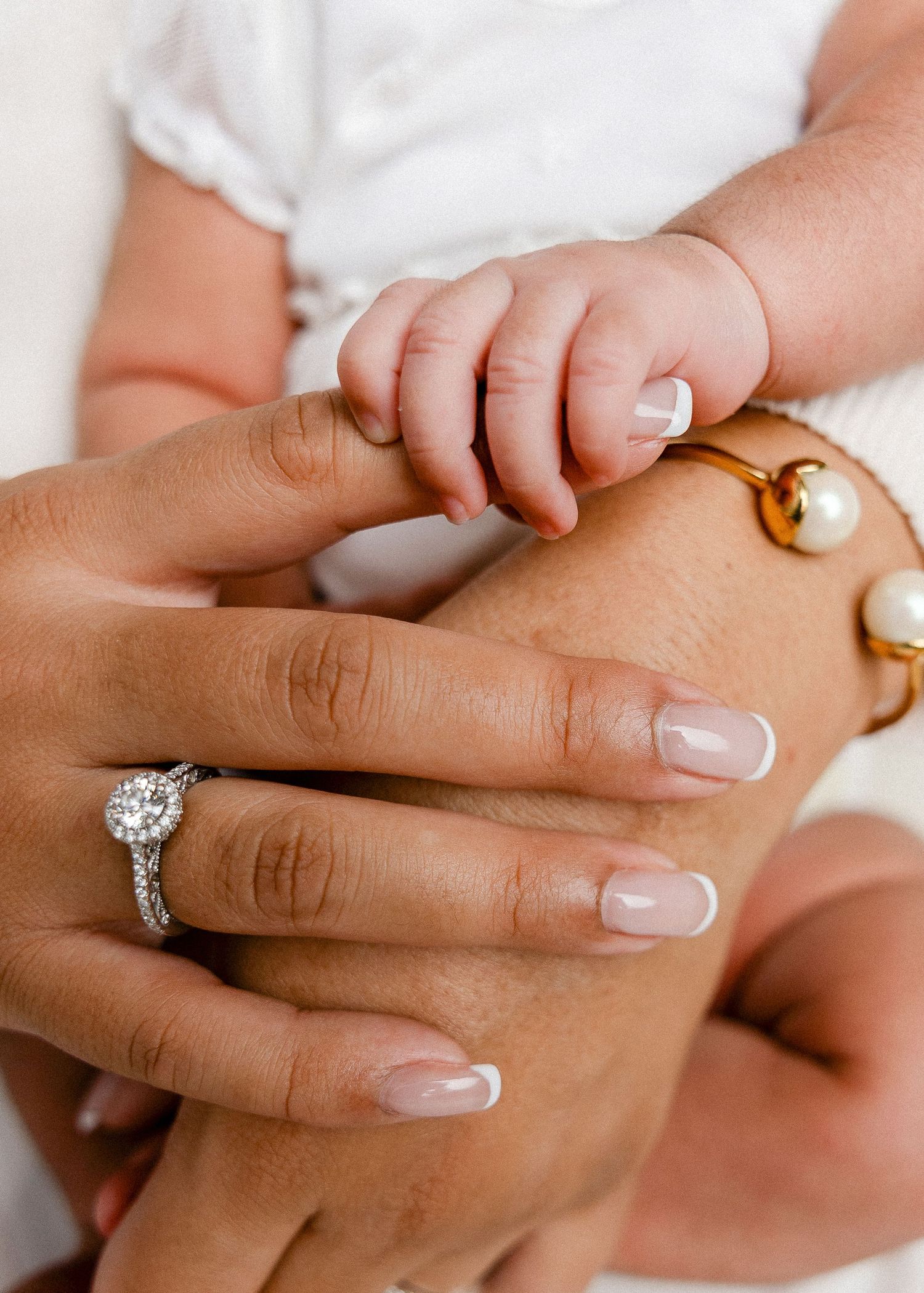 Small baby hand grasping adult finger with engagement ring visible.