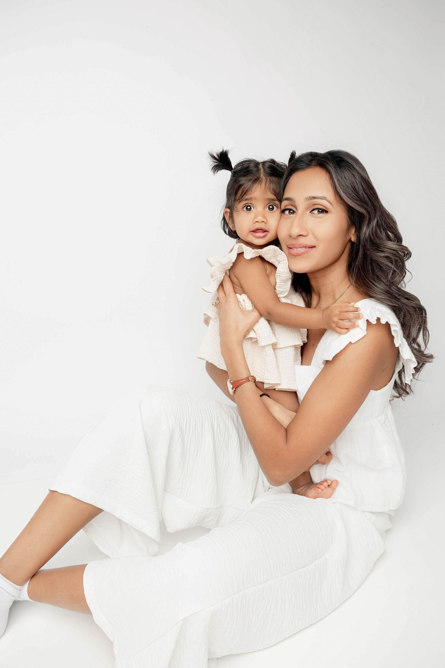 Tender moment captured in all-white outfits against clean studio background.