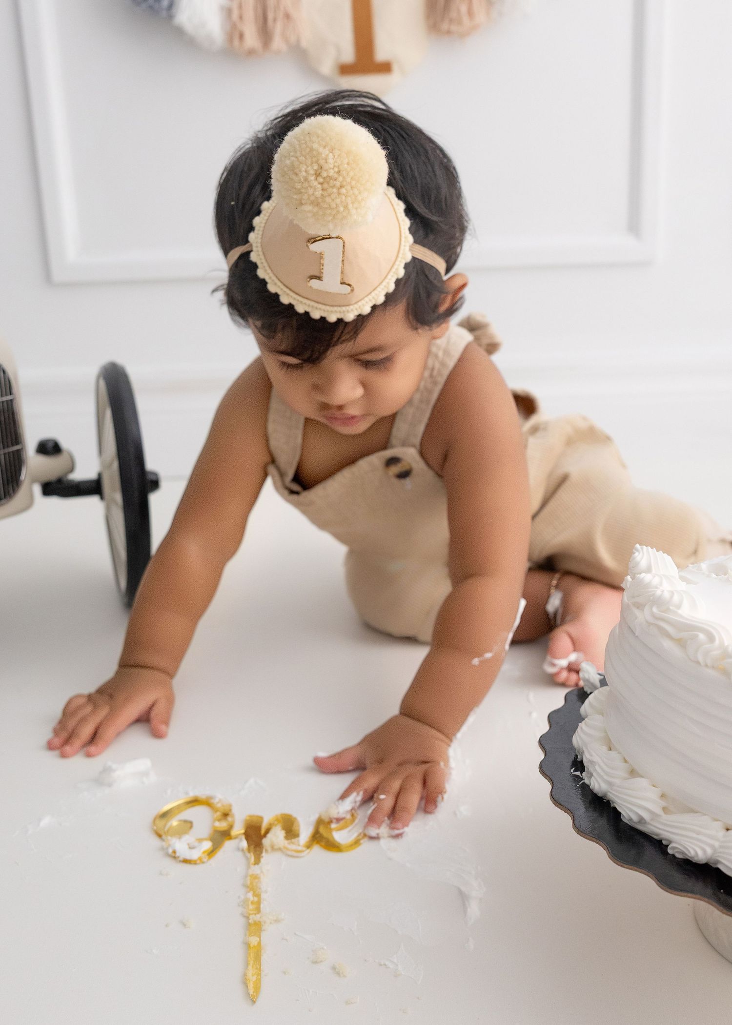 One-year-old in cream outfit playing with gold lettering on white floor.