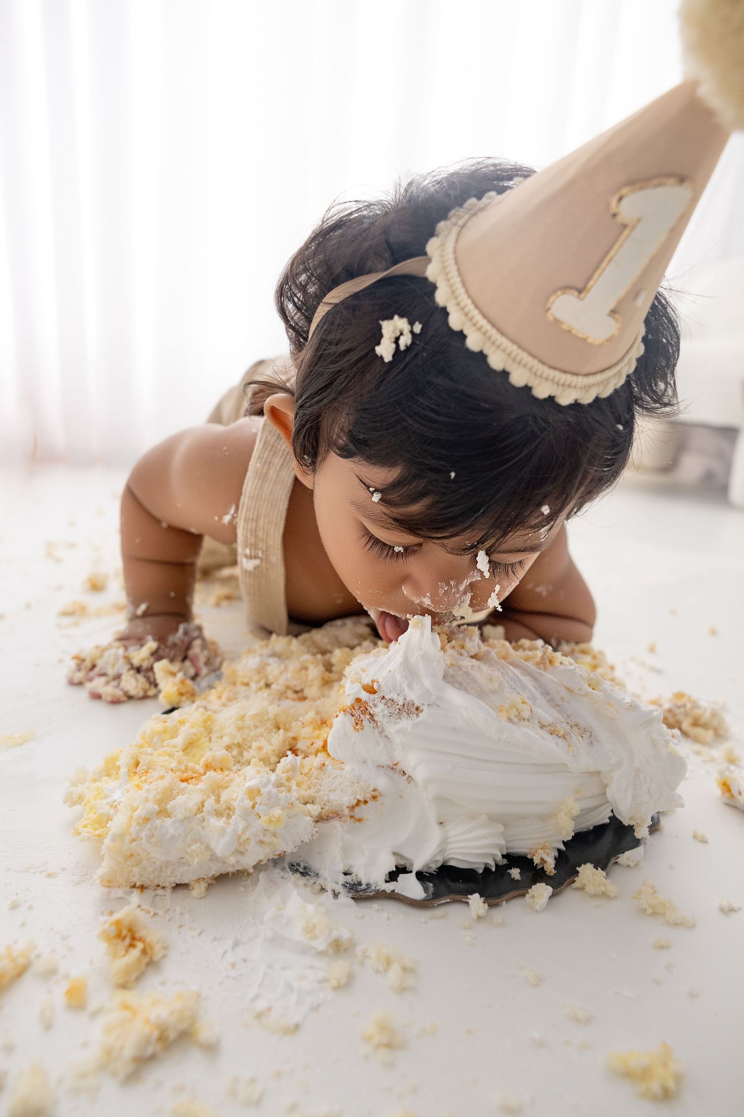 Baby lying down and tasting cake during messy cake smash photoshoot.