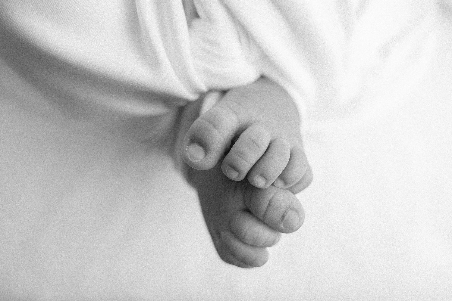 Gentle detail shot of tiny baby fingers against white fabric.
