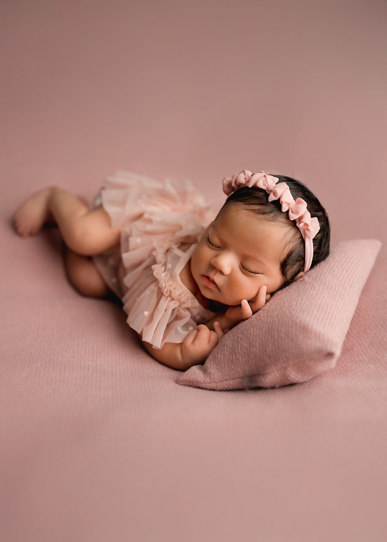 Newborn photography series on pink backdrop with delicate tulle wrap.