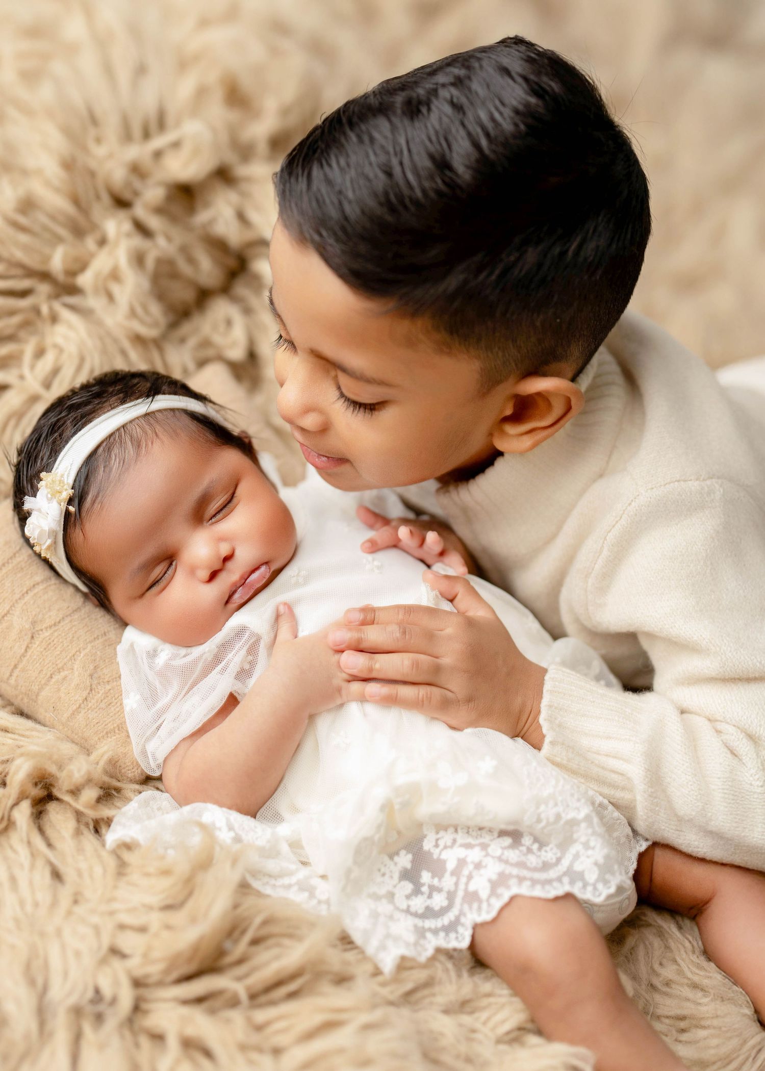 Tender sibling moment captured on cream textured blanket in soft natural light.