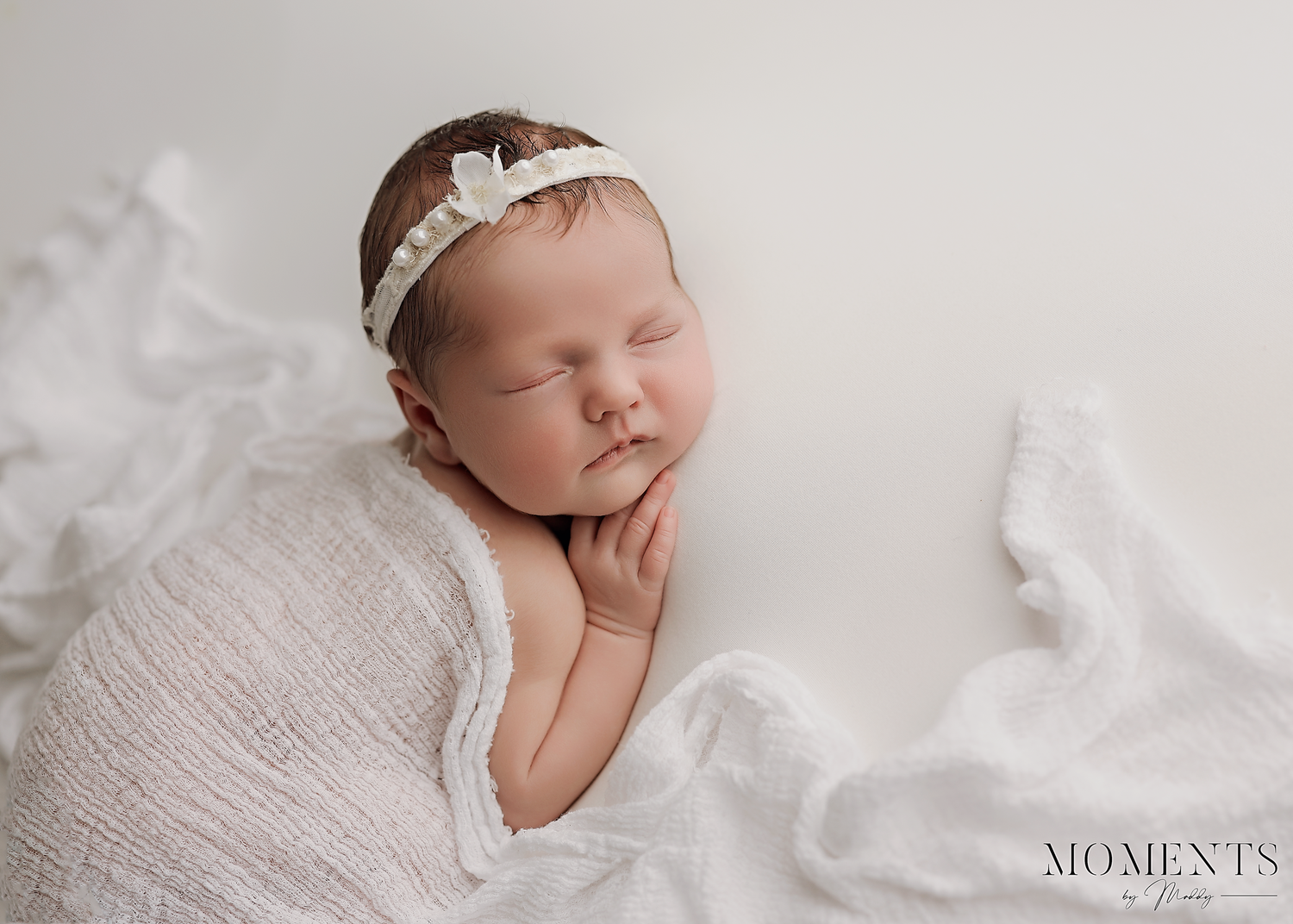 Peaceful newborn baby sleeping on white blanket wearing delicate headband.