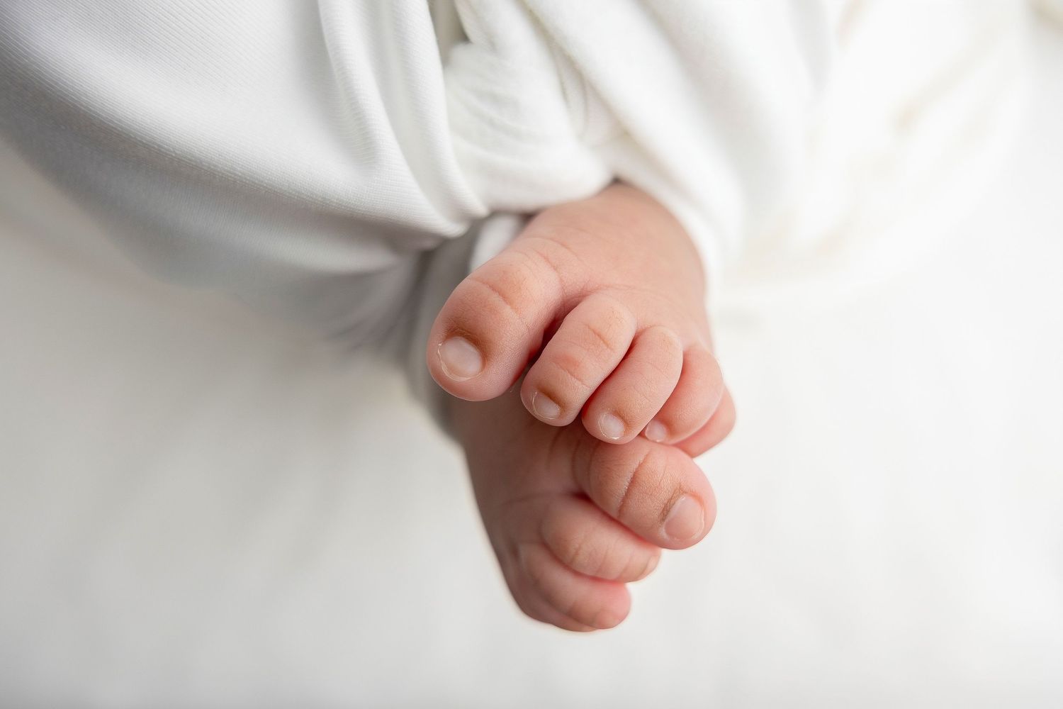Close-up detail of tiny baby feet in white clothing against light background.
