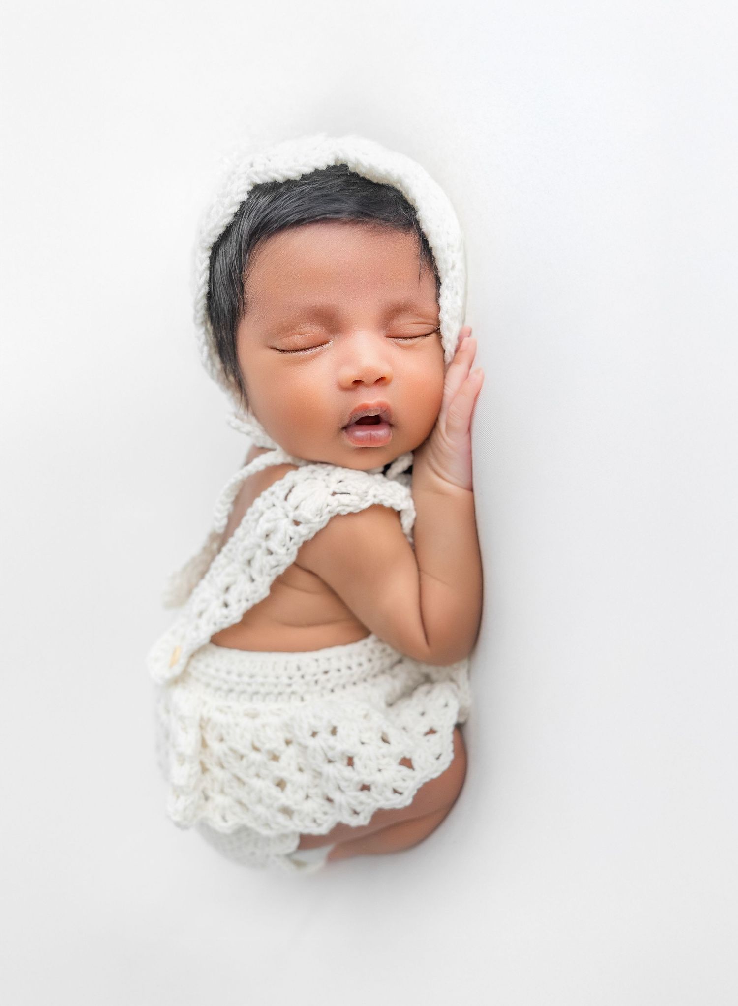 Artistic series of sleeping baby in white crochet outfit against white backdrop.