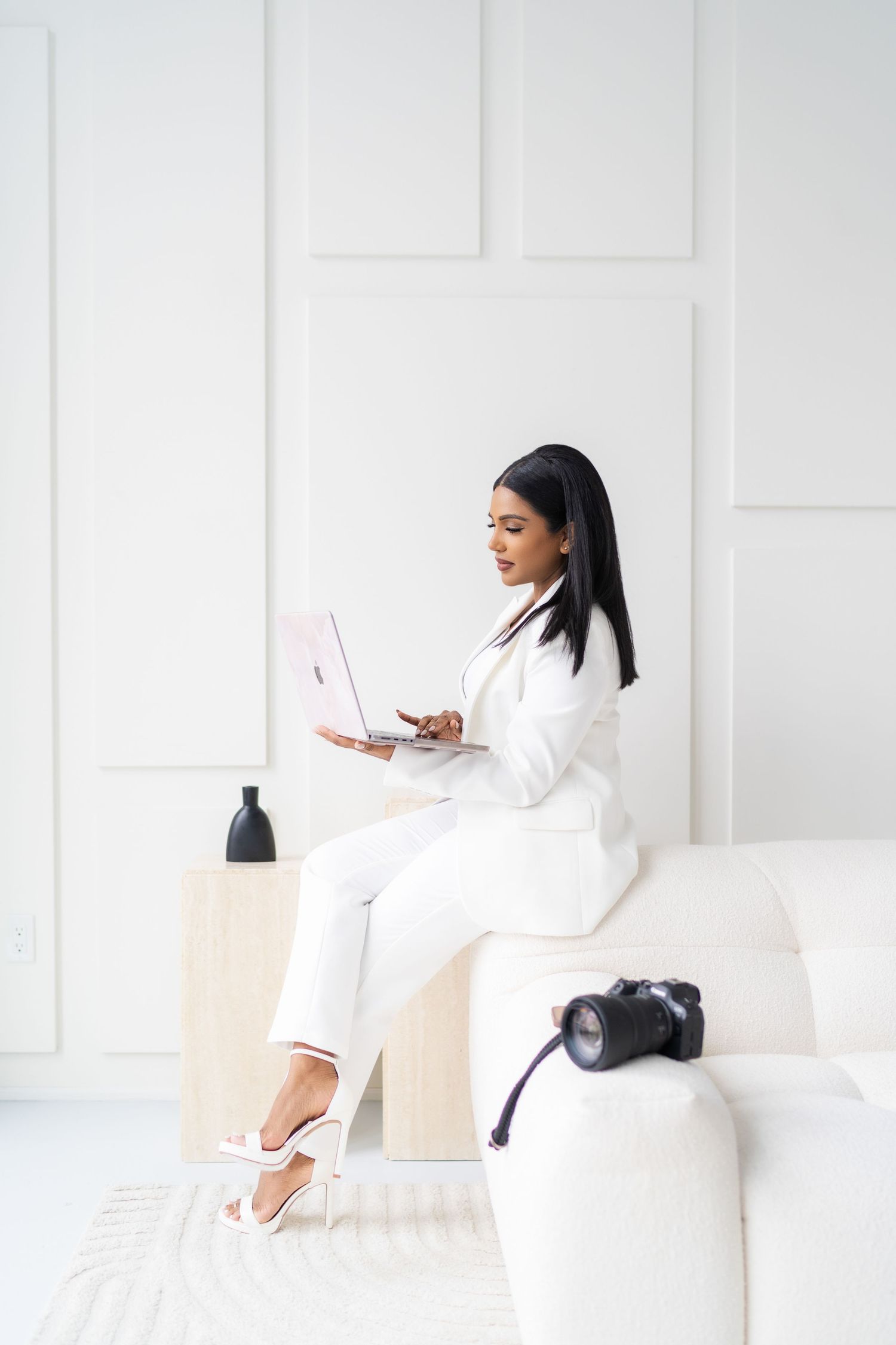 Woman in white loungewear working on laptop in bright modern room.