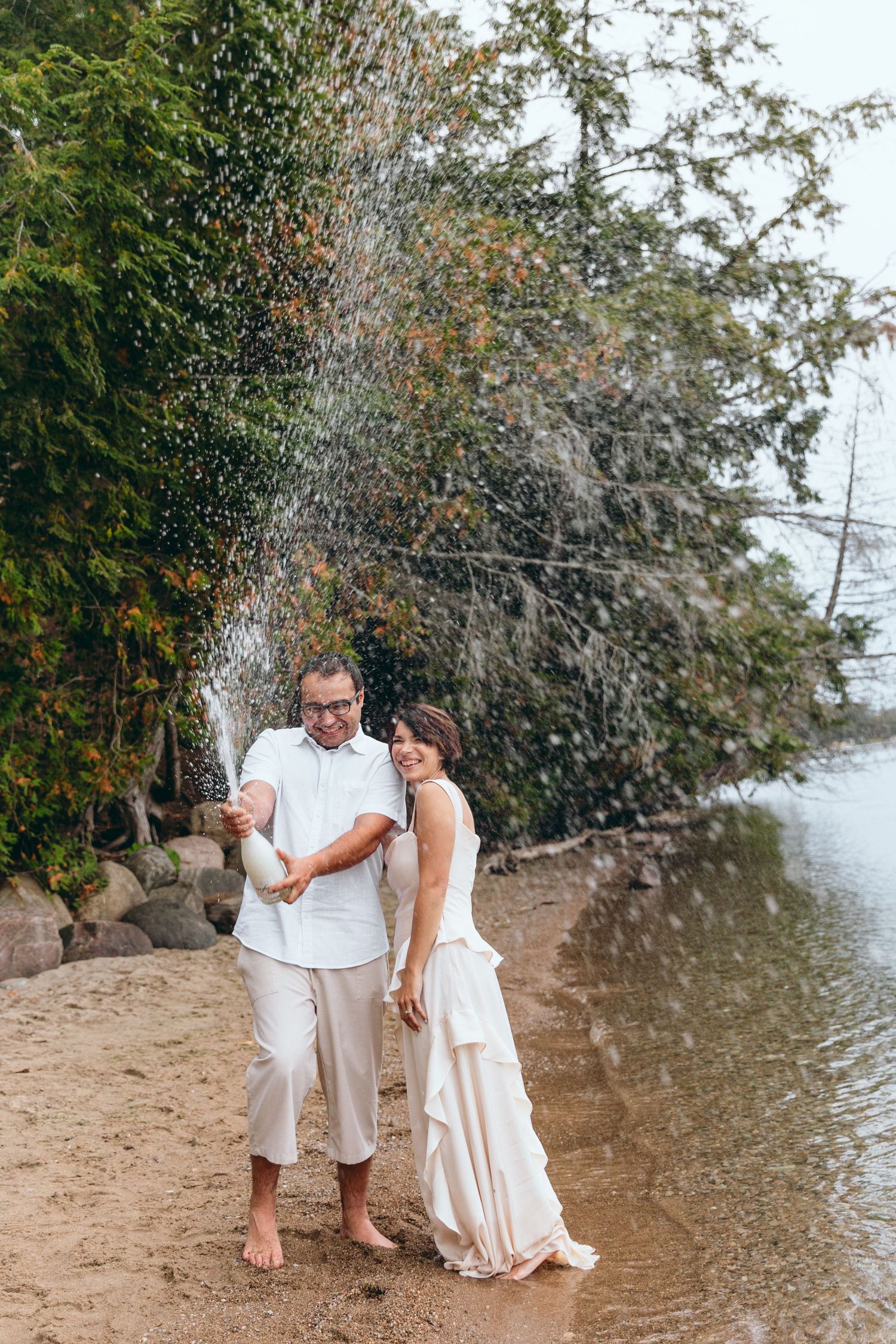 Playful beach photoshoot with water splashing near rocky shoreline.
