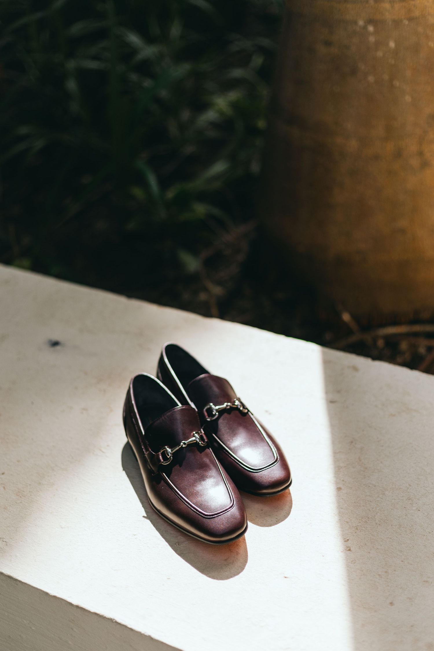 Brown leather loafers in natural sunlight on white surface.