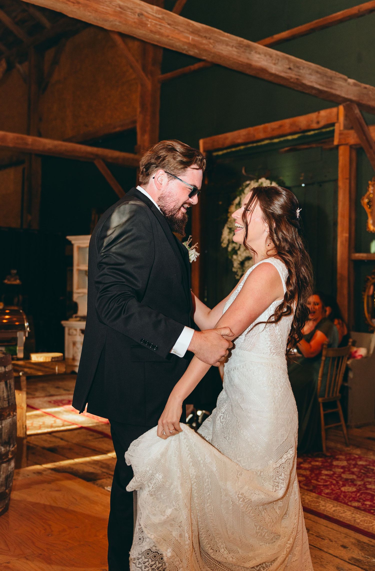 Romantic first dance moment in rustic barn venue with wooden beams.