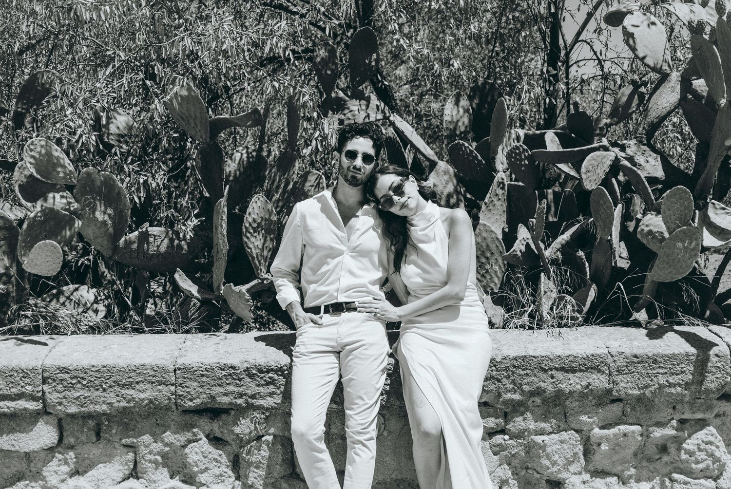 A romantic black and white photo of a couple sitting on an ancient stone wall.