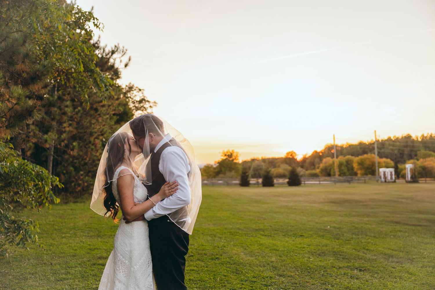 Newlyweds embrace during golden hour in a scenic outdoor field setting.