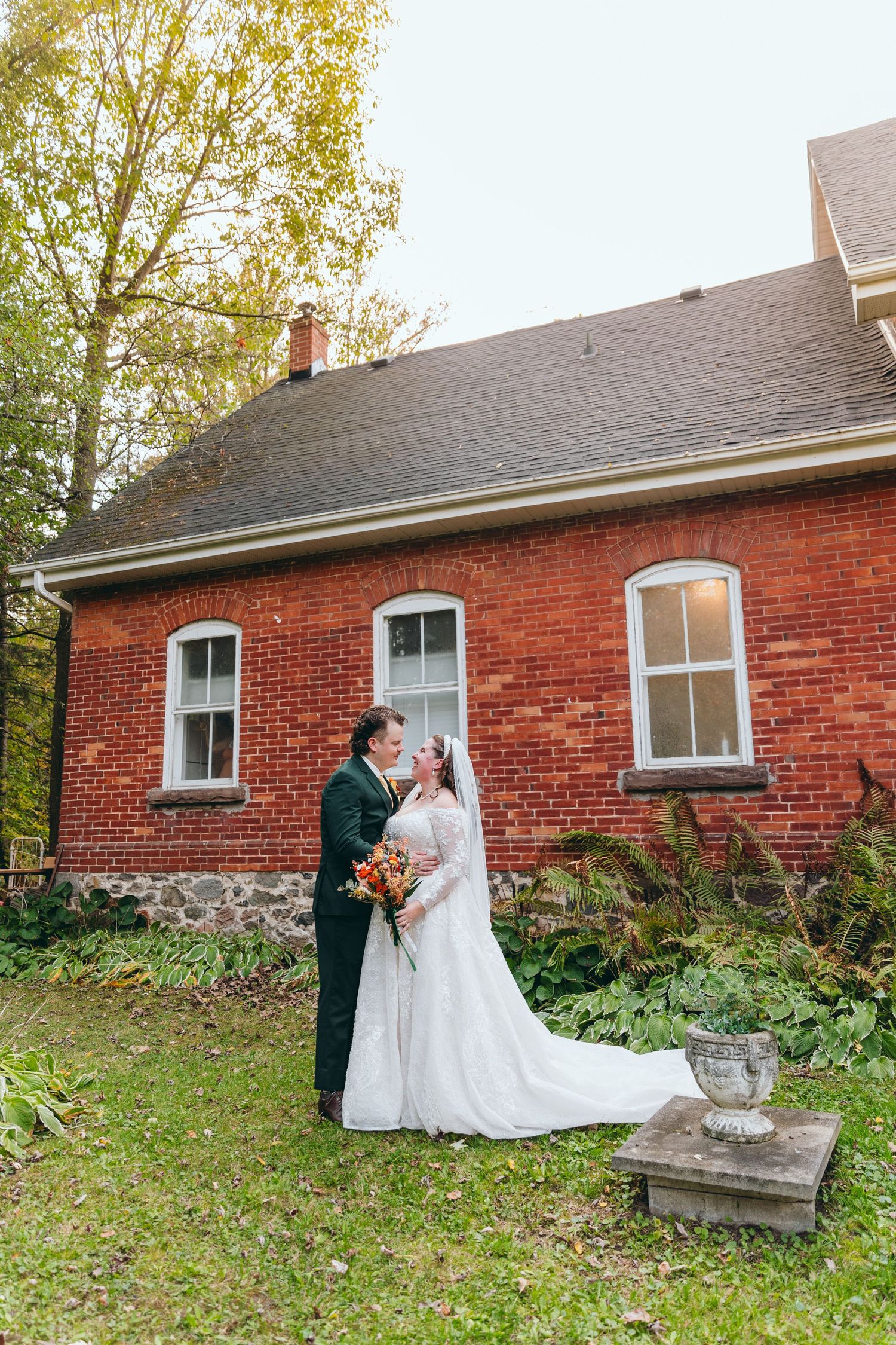 Wedding couple poses in front of red brick building during autumn.
