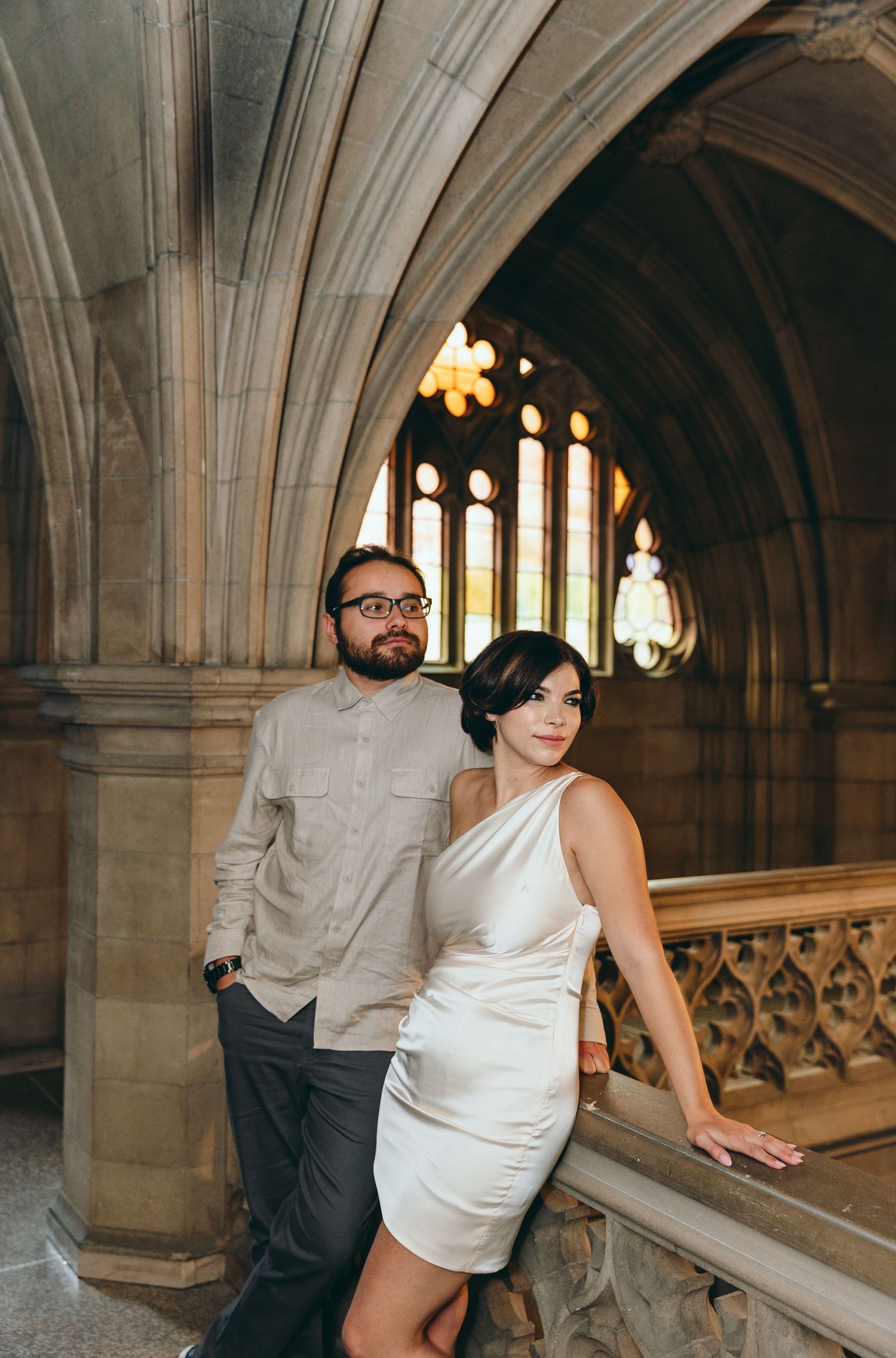 Couple poses playfully in a Gothic architecture setting with arched windows and stone columns.