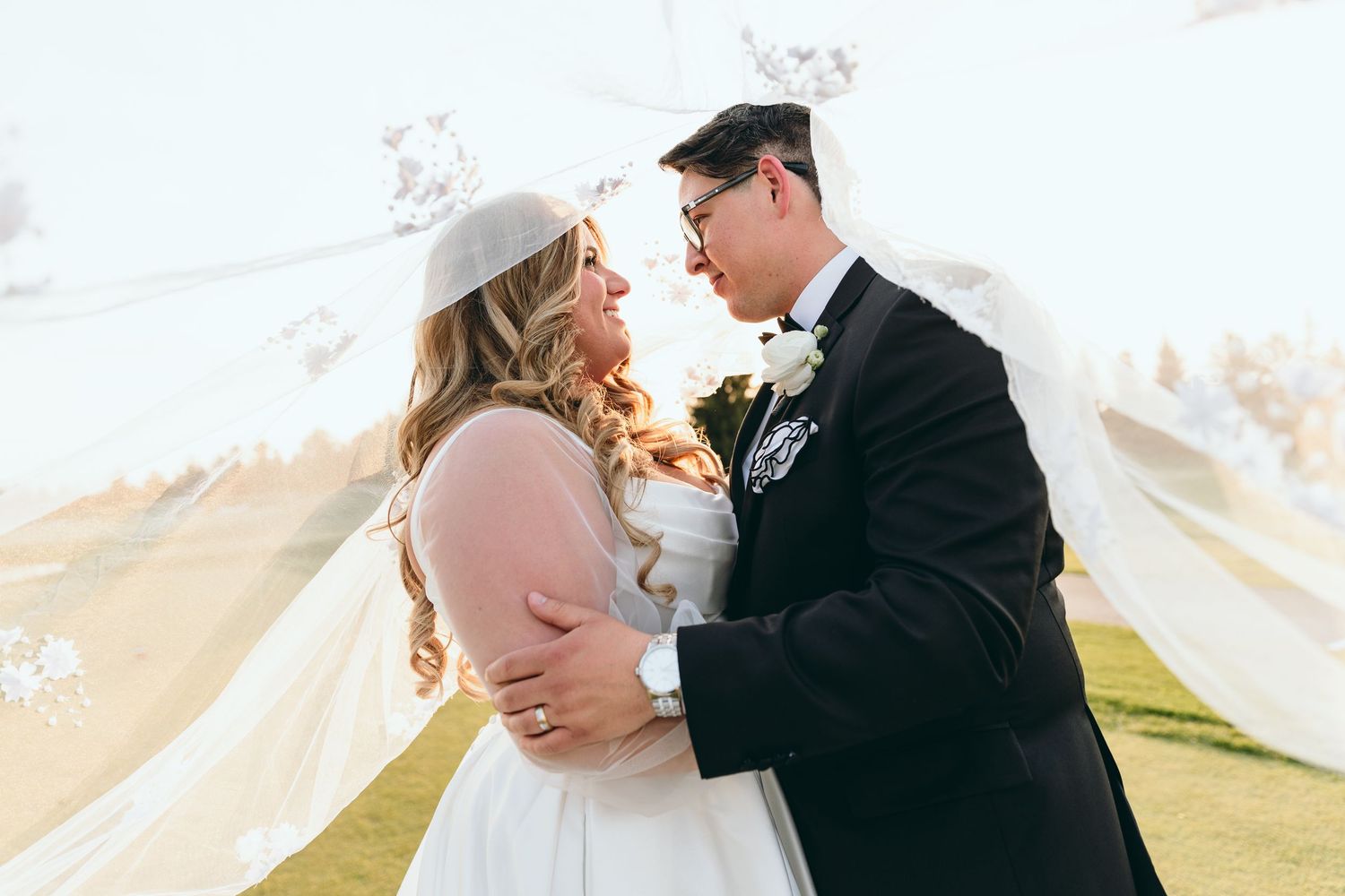 A tender moment between newlyweds with a flowing veil against a scenic outdoor backdrop.