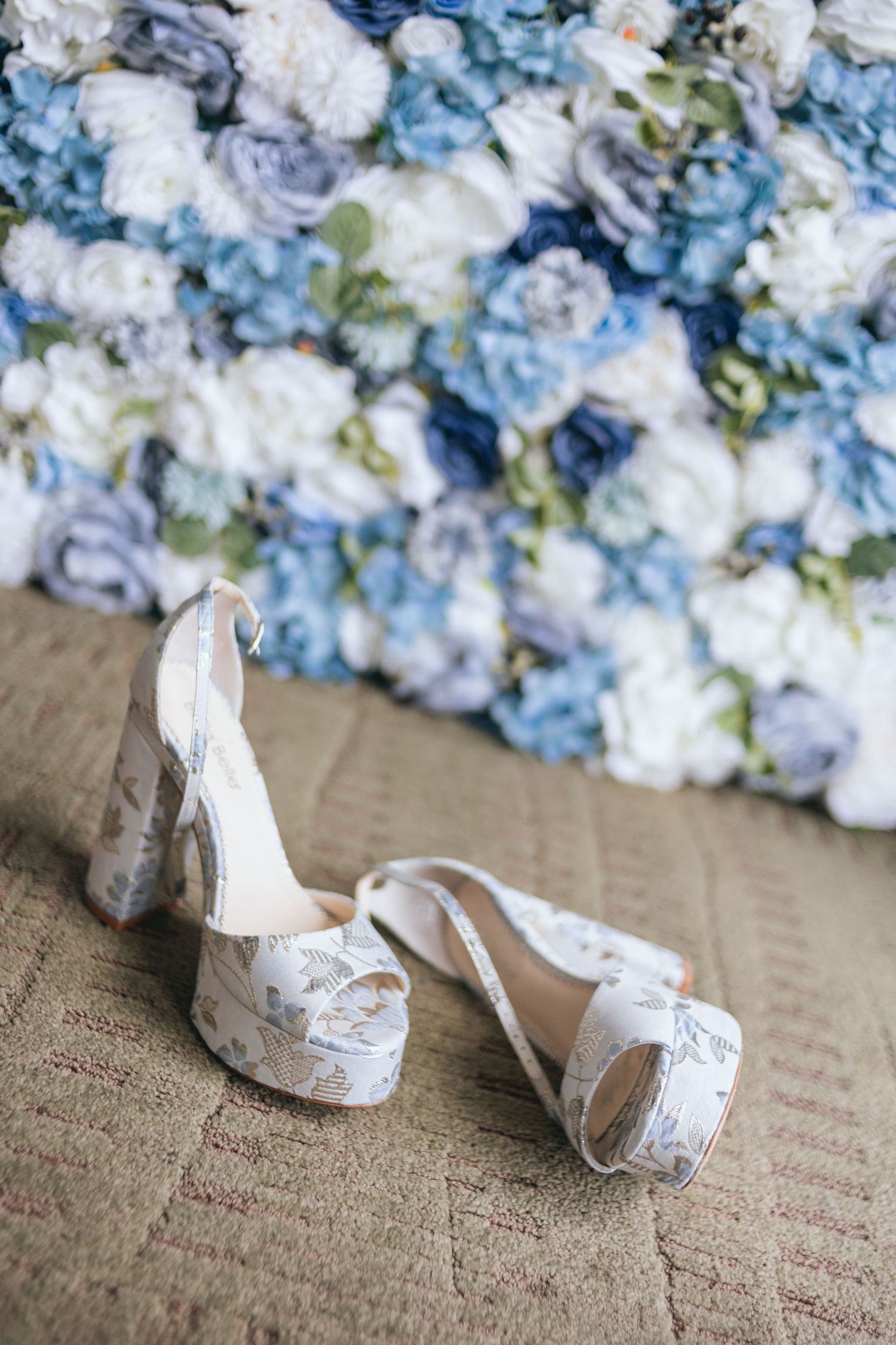 White and blue floral arrangements with bridal shoes on textured carpet.