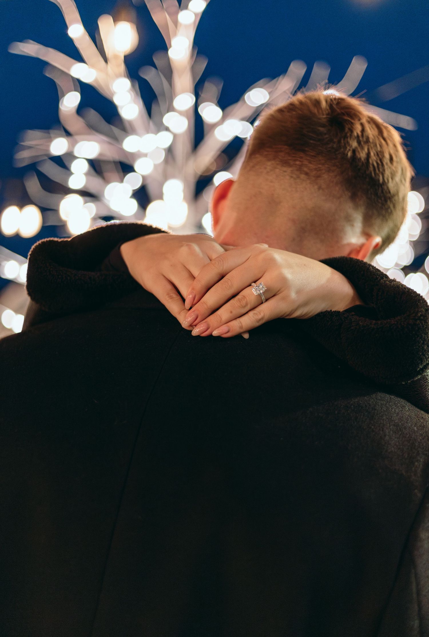 Intimate embrace captured against a backdrop of twinkling lights at night.