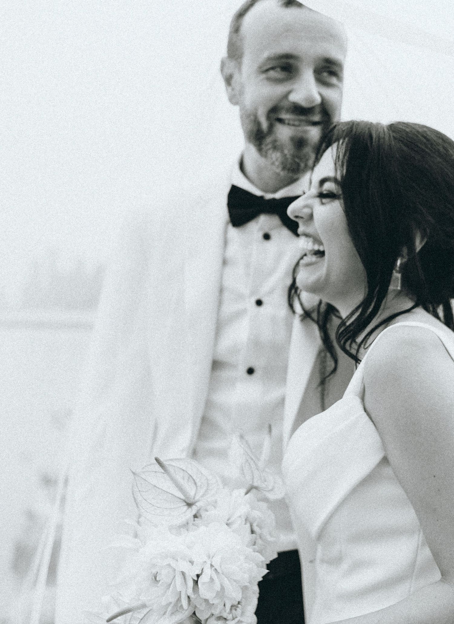 A joyful black and white wedding photo showing a laughing couple in formal attire with a bouquet.