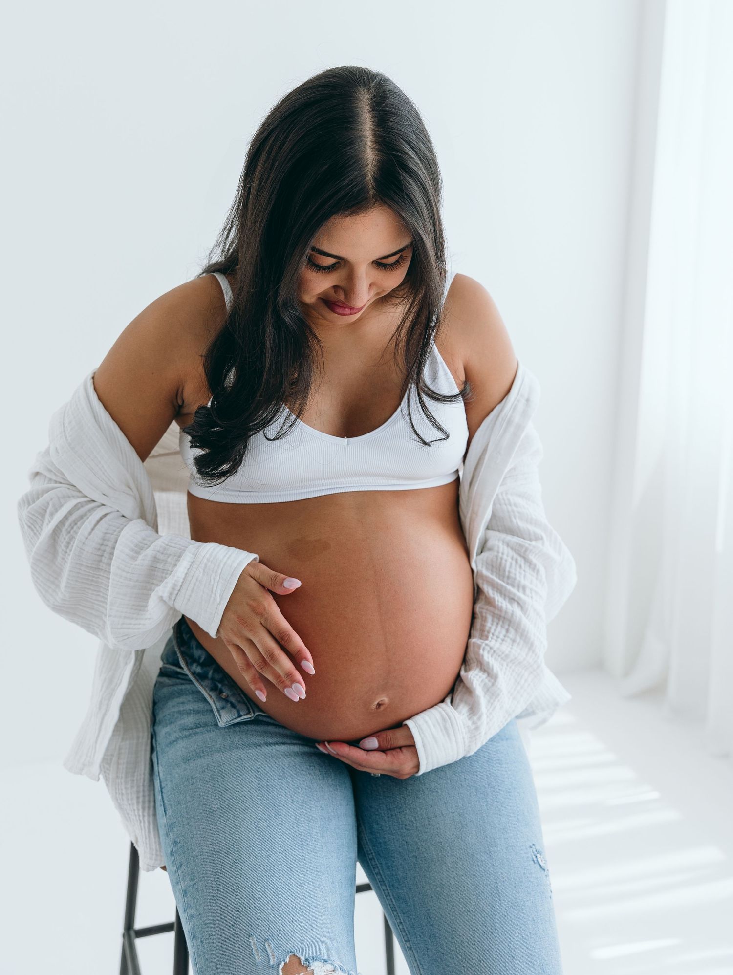 Artistic pregnancy photo with woman cradling baby bump in bright studio.